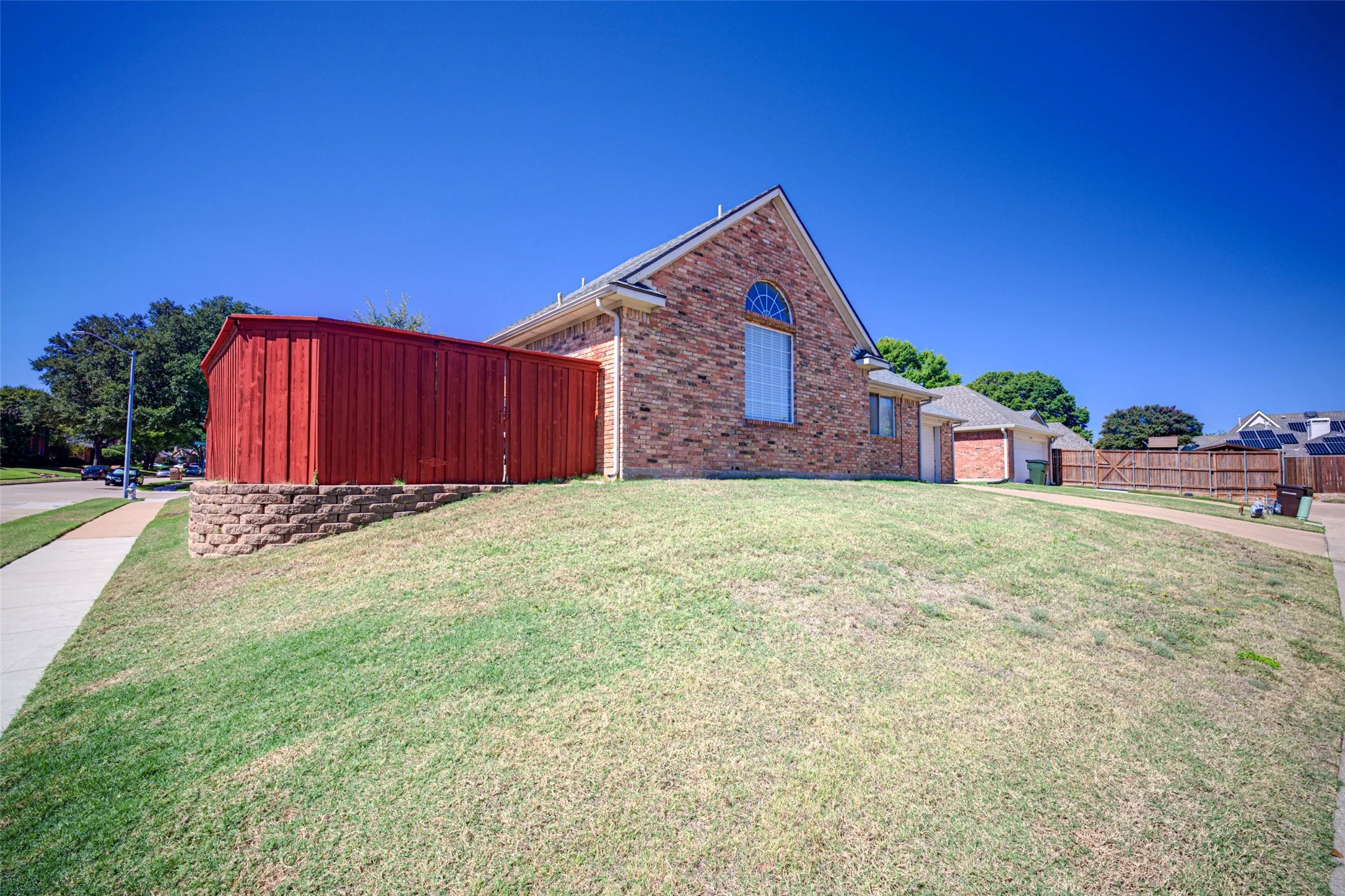 Brick exterior featuring an arched window, attached garage, and a wood privacy fence
