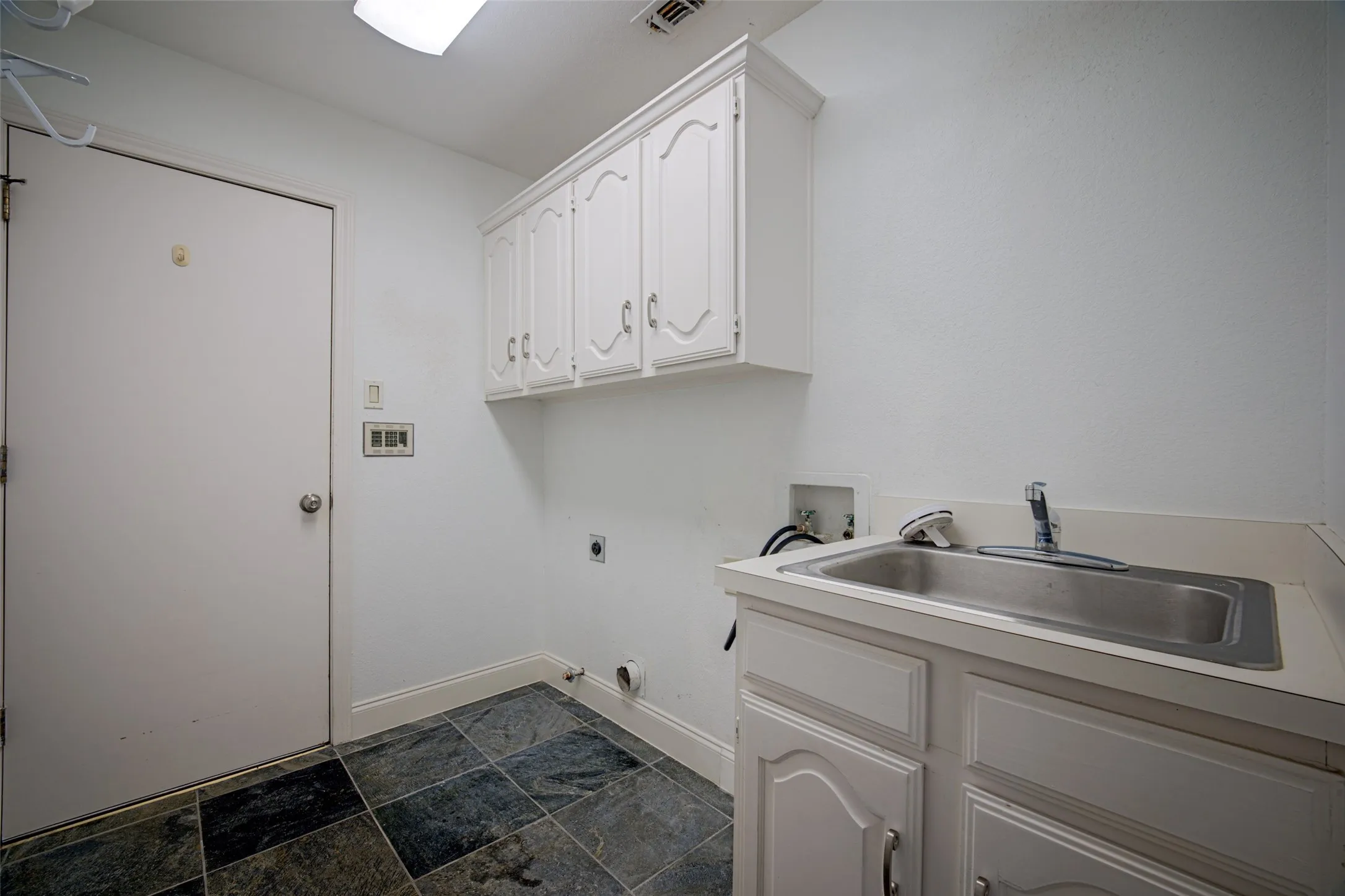 Laundry area with a utility sink, white cabinetry, and multi-toned tile flooring