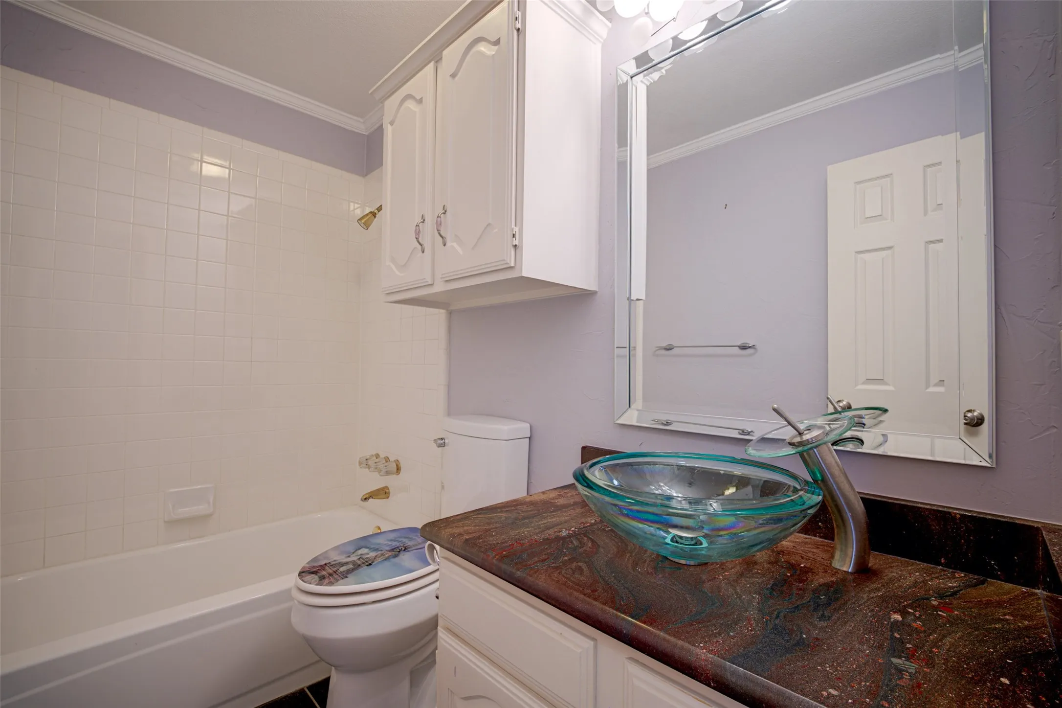 White tile-surround bathtub, glass vessel sink, mounted mirror, and built-in white cabinetry