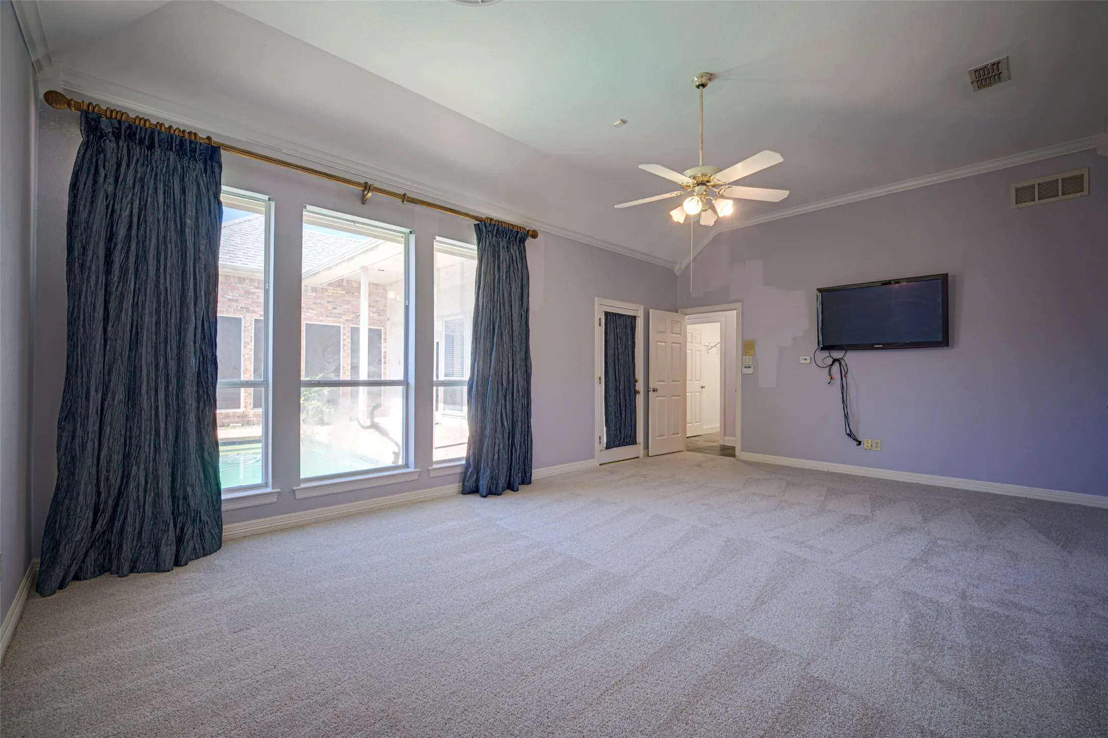 Primary bedroom Vaulted ceiling with crown molding, ceiling fan with light fixture, light gray carpet, and multiple windows