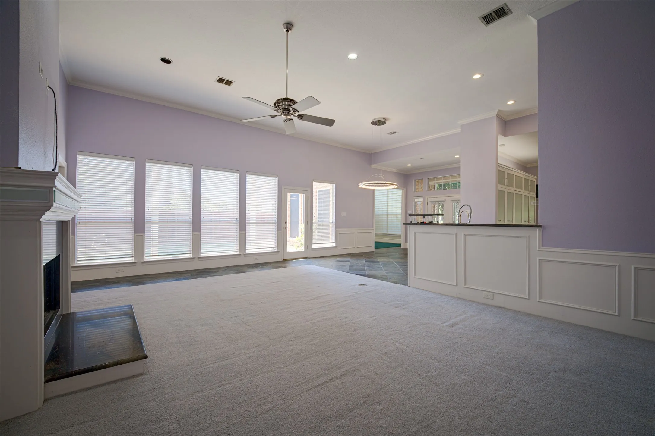 Vaulted ceiling with recessed lighting and a ceiling fan, fireplace with a dark stone hearth, a wall of windows, and a built-in bar with a dark countertop and sink