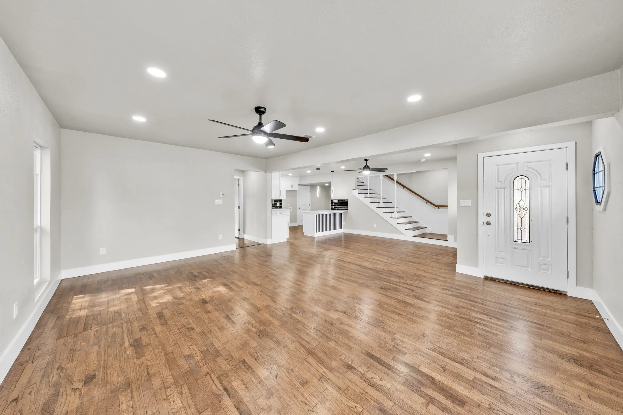 Hardwood flooring, recessed lighting, ceiling fan, white paneled entry door with decorative glass, and a staircase with white risers and wood-finish treads