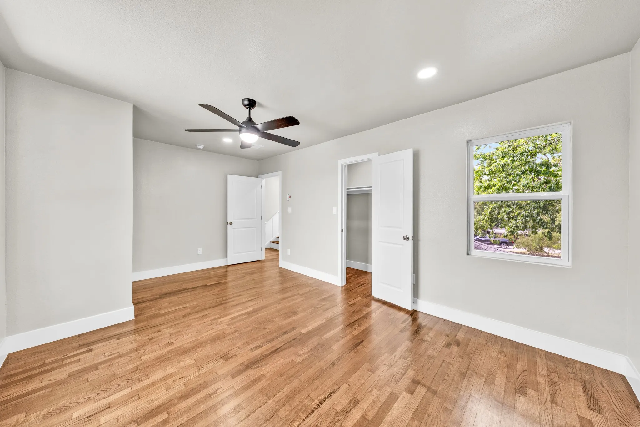 Hardwood flooring, recessed lighting, ceiling fan, white trim, and a window with outdoor greenery