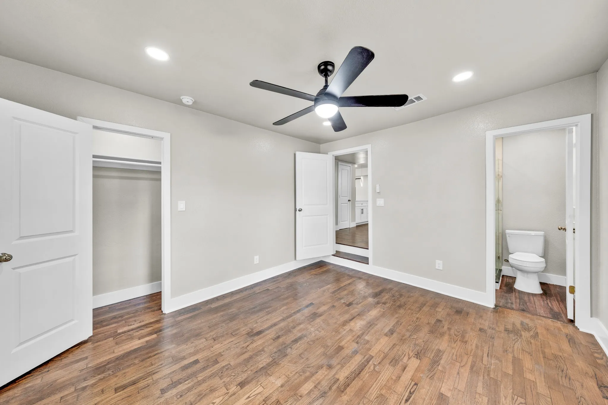 Wood-finish flooring, recessed lighting, matte black ceiling fan, white paneled doors, and a closet with hanging rods