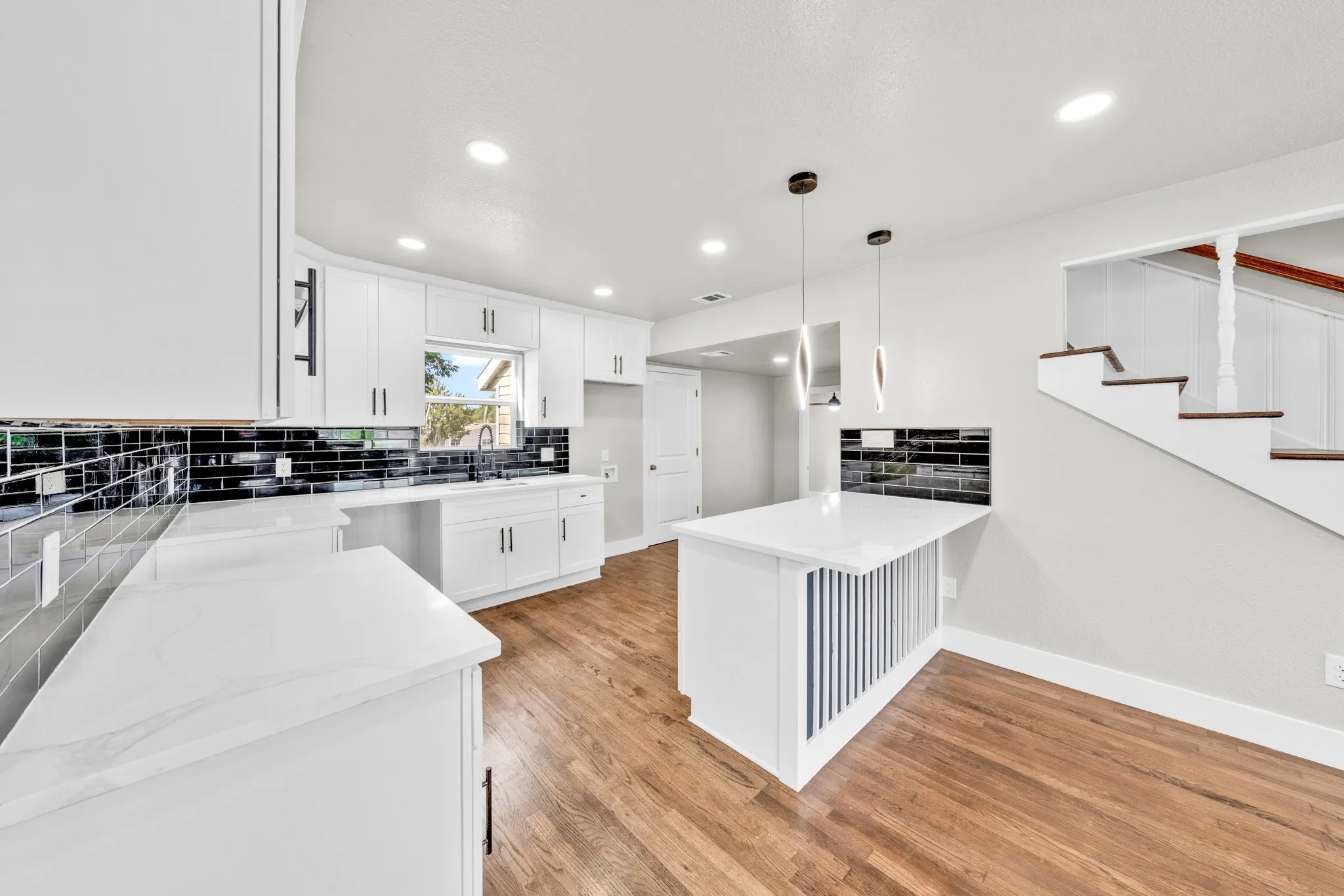 Modern kitchen featuring white cabinetry with dark hardware, black subway tile backsplash, white countertops, and wood-finish flooring