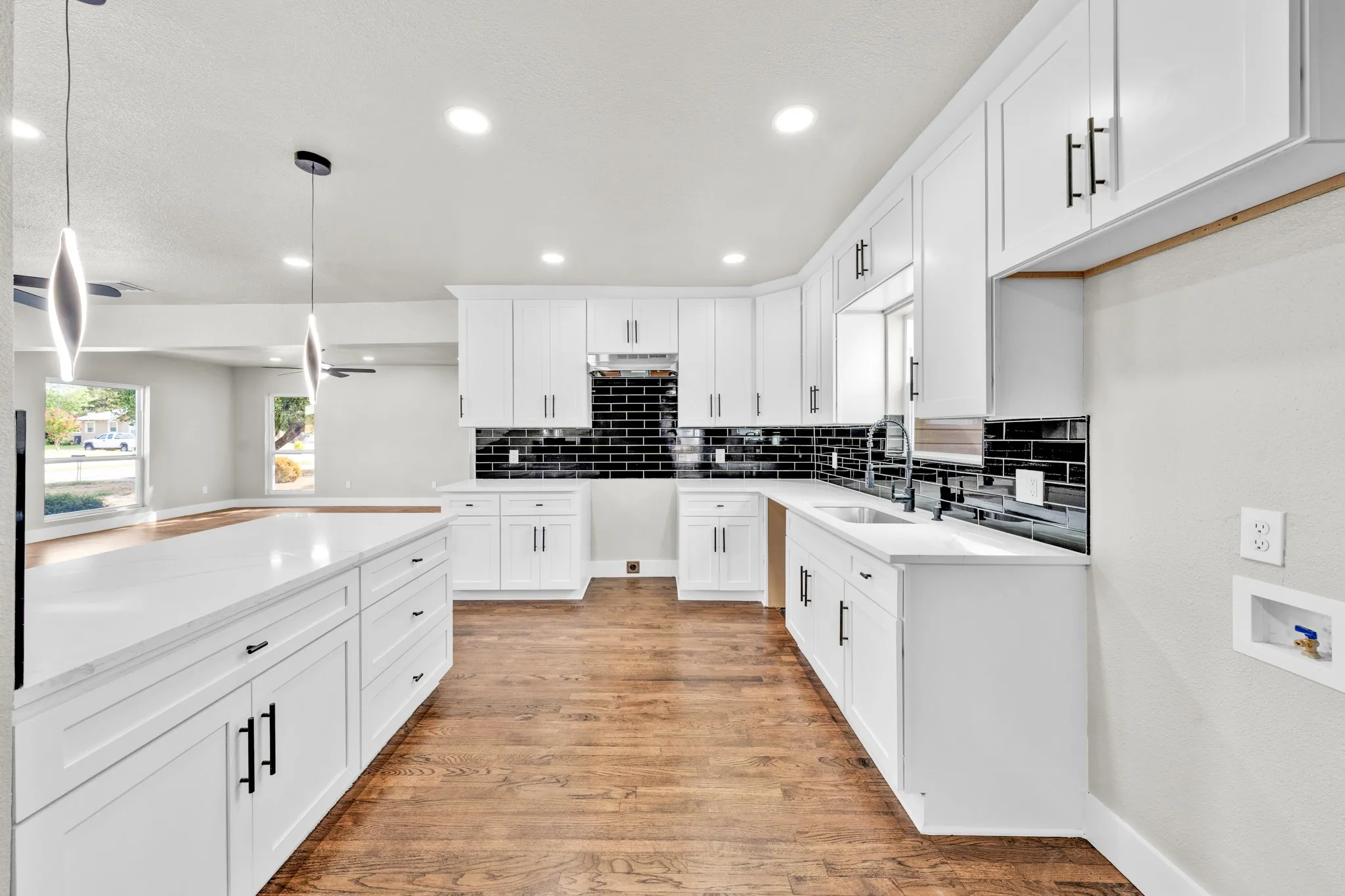 Kitchen featuring white shaker cabinetry, white countertops, black subway tile backsplash, wood-finish flooring, and a large central island