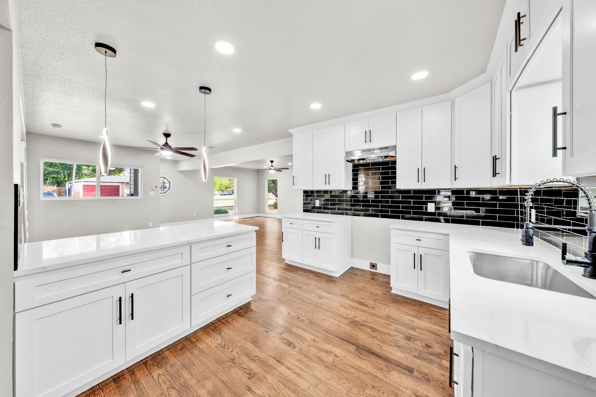 Kitchen featuring white cabinetry, black subway tile backsplash, white countertops, stainless steel sink with a black faucet, and wood-finish flooring