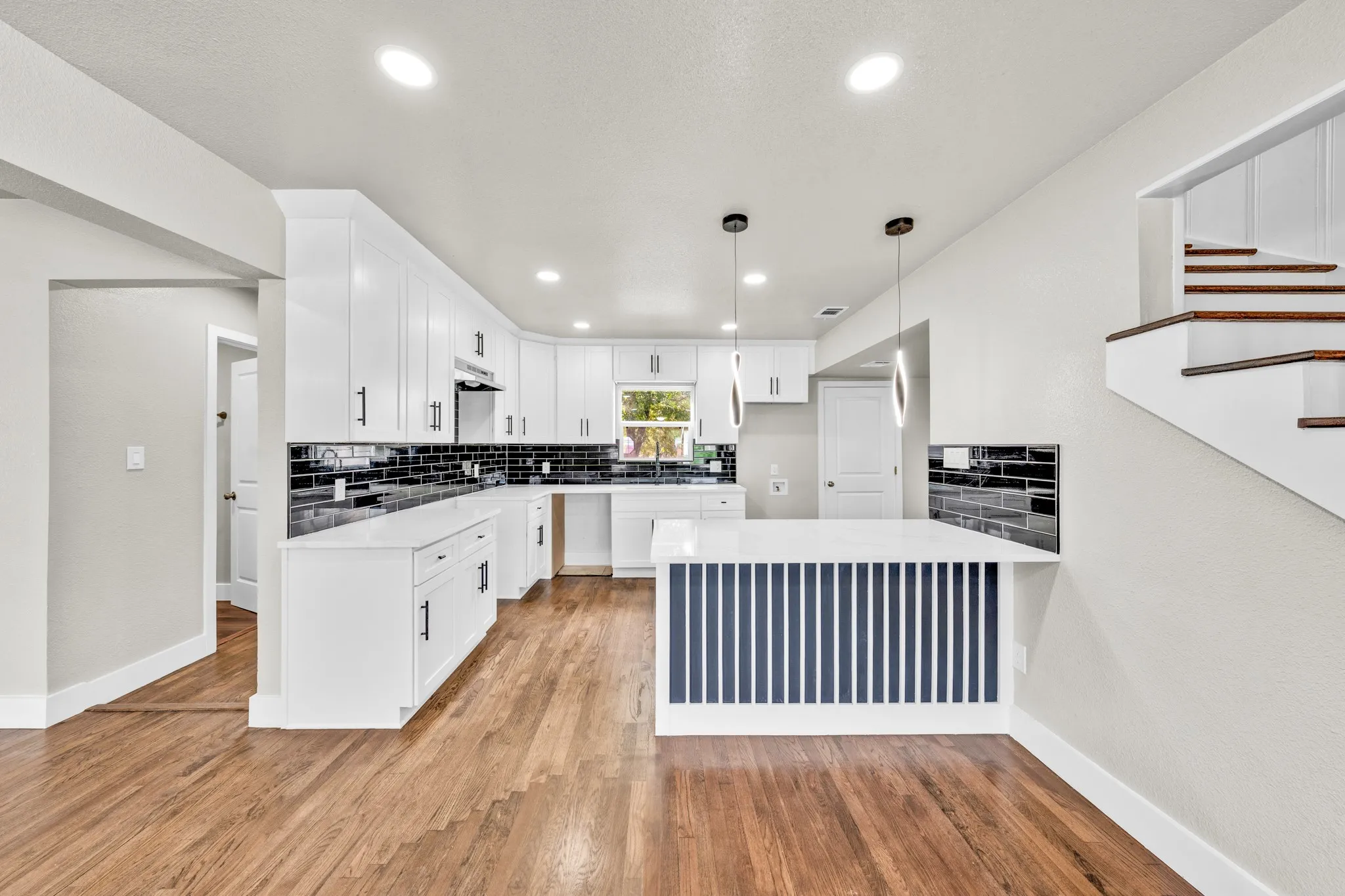 Kitchen featuring white cabinetry, dark subway tile backsplash, white countertops, and wood-finish flooring