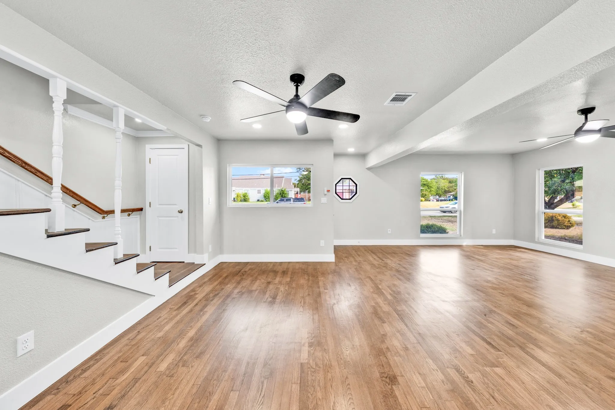 Wood-finish flooring throughout, modern ceiling fans, recessed lighting, and a staircase with wood treads and white risers