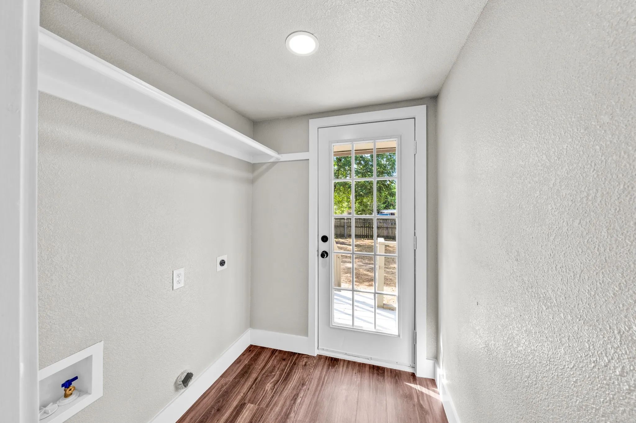 Laundry area with wood-finish flooring, built-in shelving, and a glass-paned door