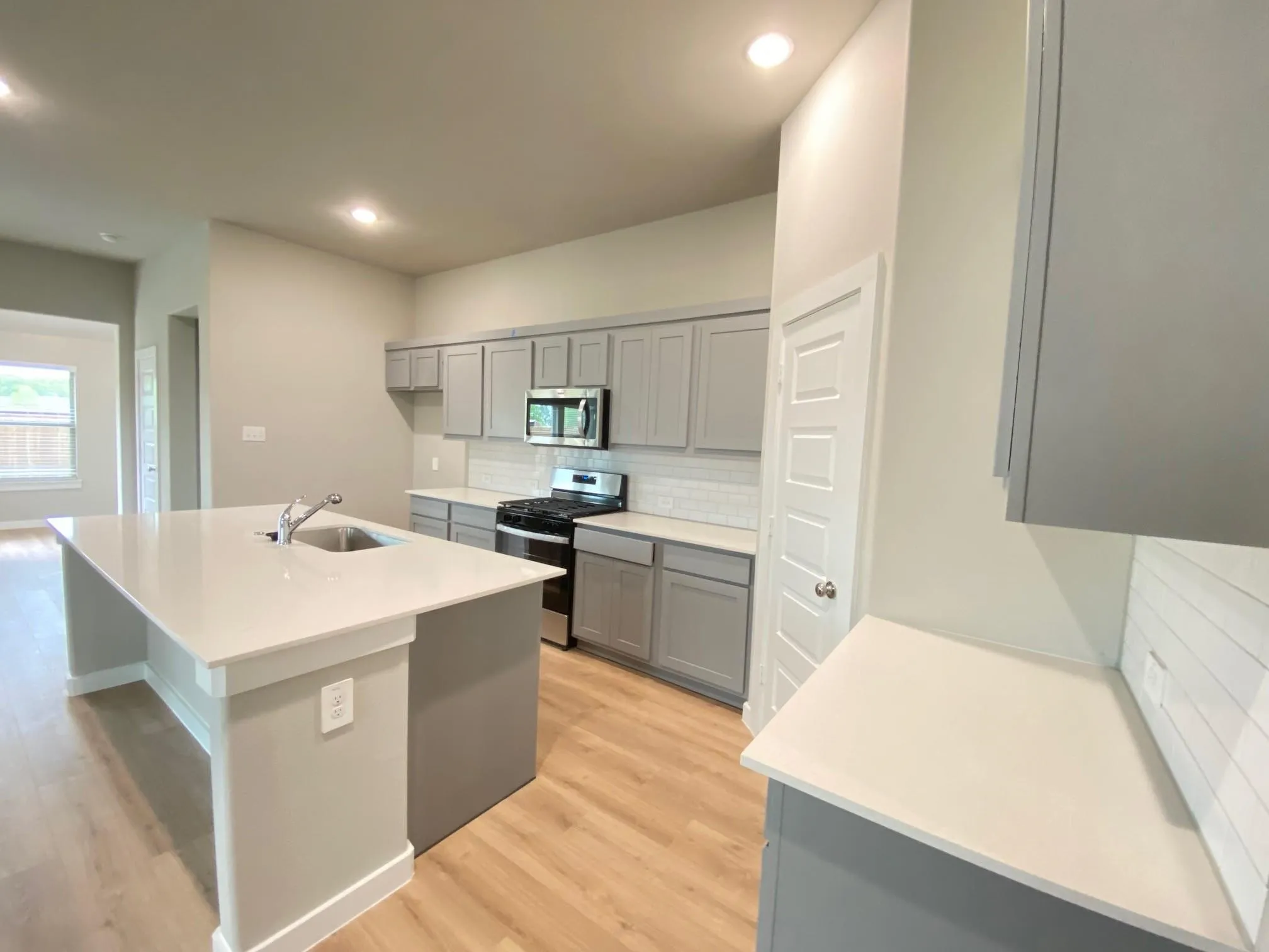 Kitchen featuring a large island with an integrated sink, light wood-finish flooring, recessed lighting, gray cabinetry, and white countertops