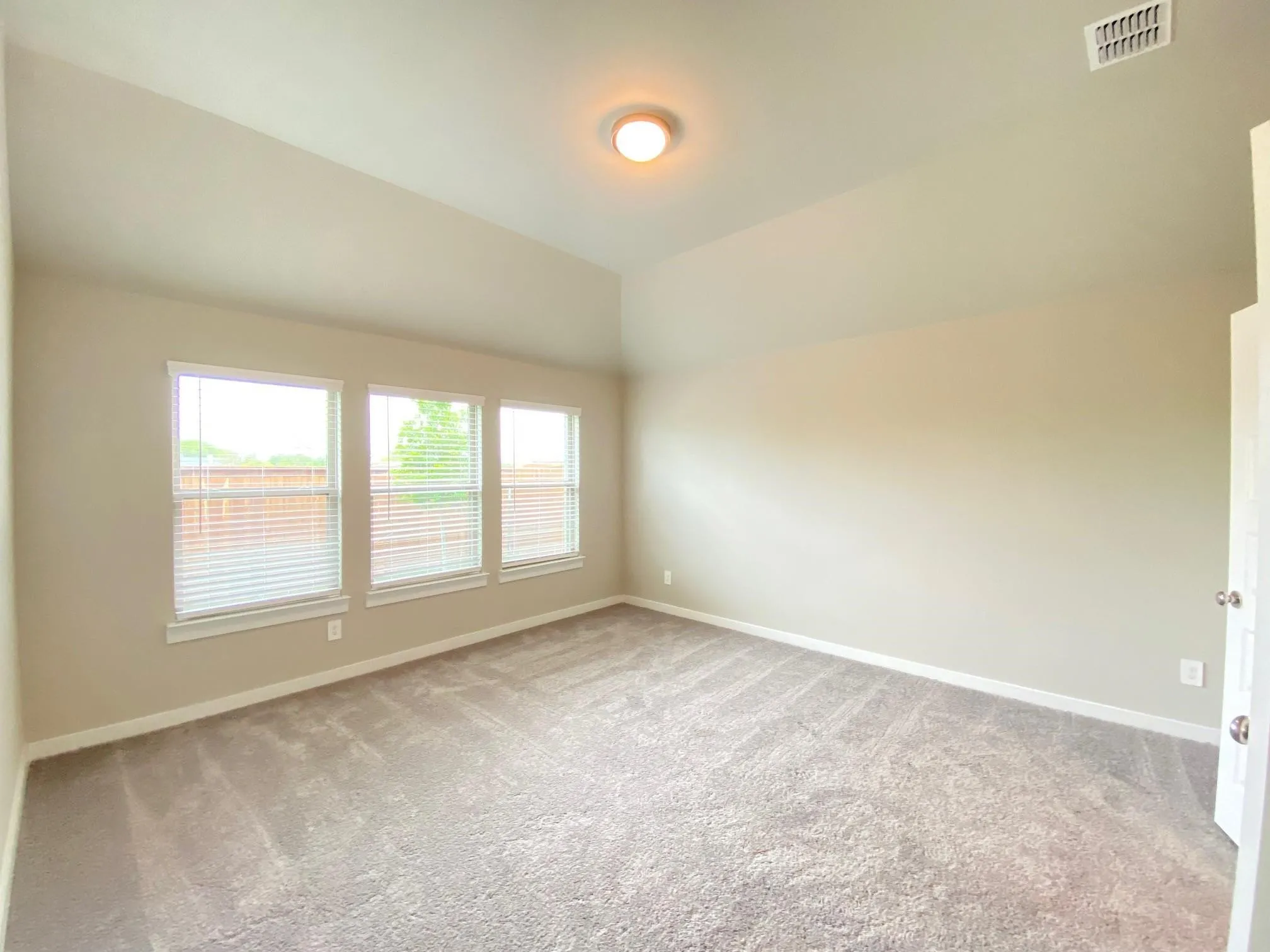Vaulted ceiling, three windows, textured carpet, ceiling-mounted light fixture, and neutral wall paint