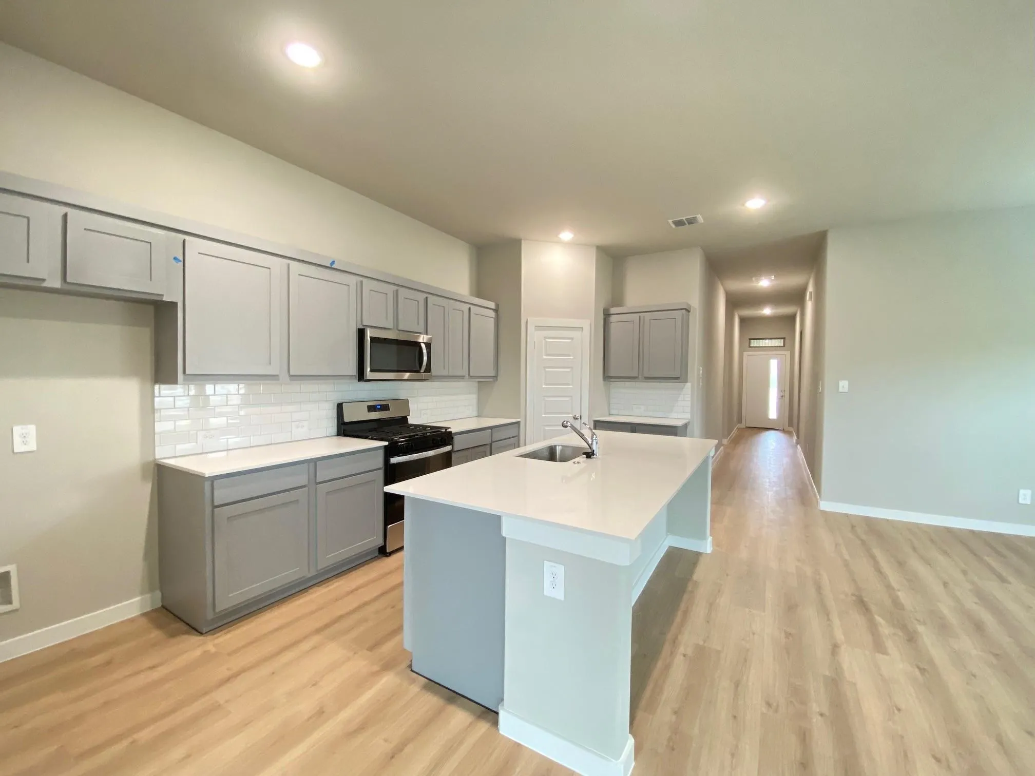 Kitchen featuring a large central island with an undermount sink, light-colored cabinetry, stainless steel appliances, a subway tile backsplash, and recessed lighting