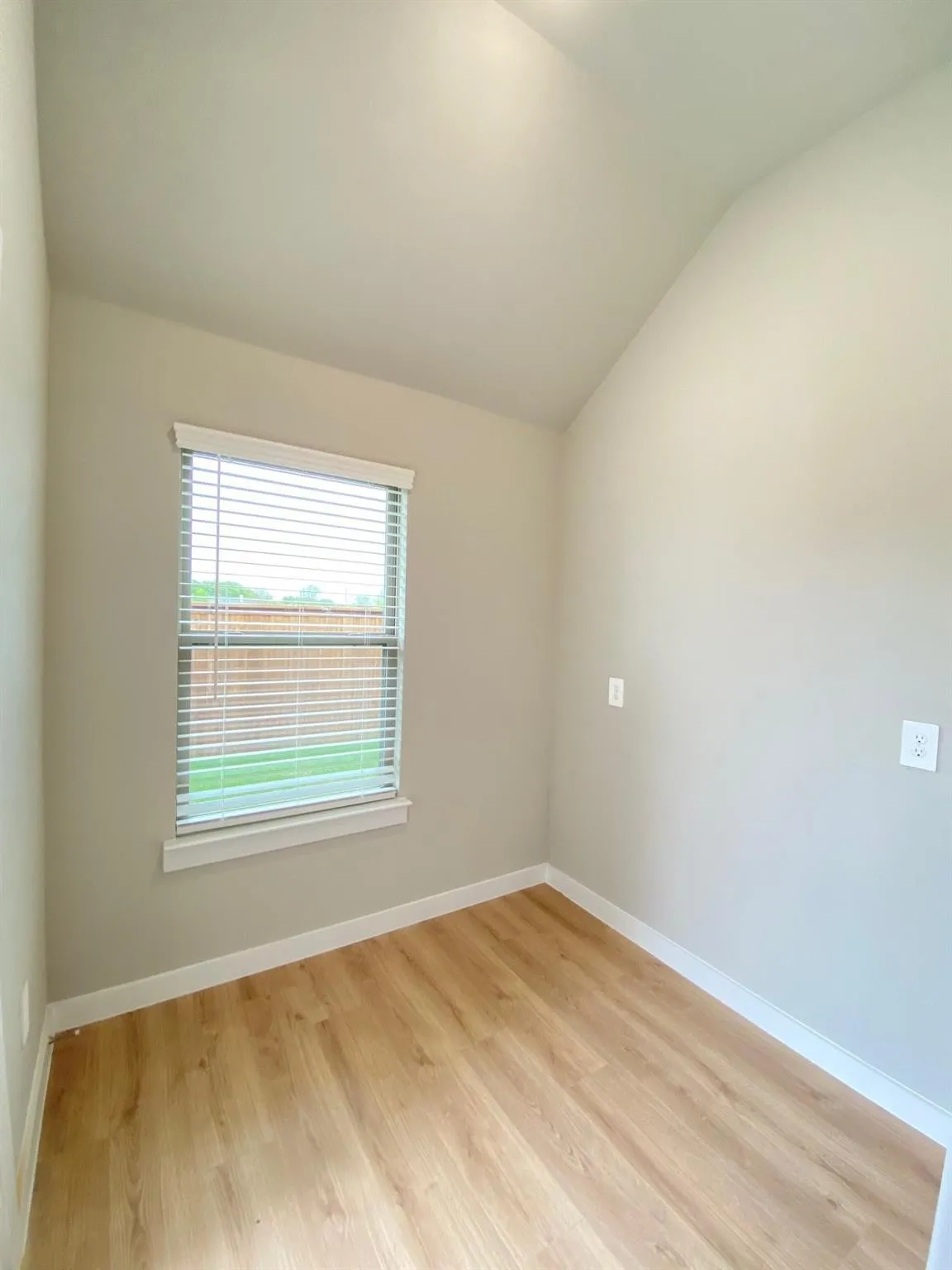 Vaulted ceiling, wood-finish flooring, neutral paint palette, window with blinds, and white trim