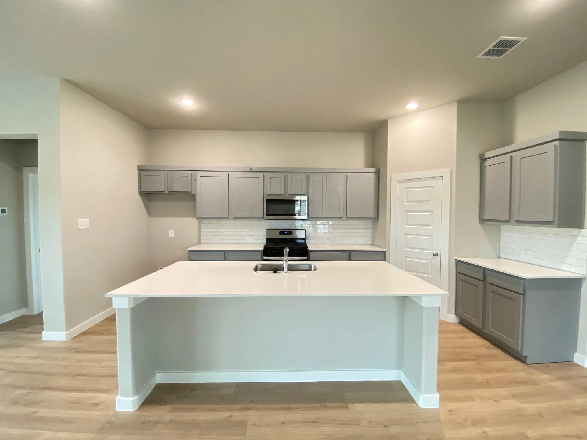 Kitchen featuring an expansive island with a sink, grey cabinetry, white countertops, subway tile backsplash, and wood-finish flooring