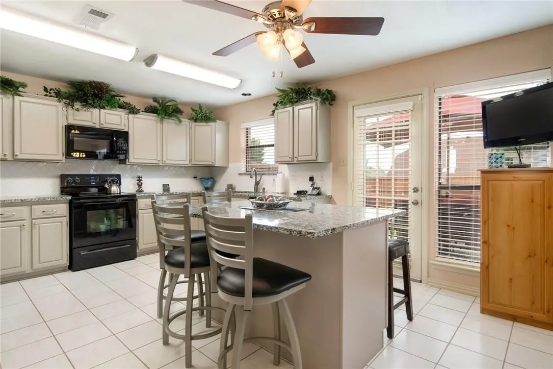 Kitchen featuring light-toned cabinetry, granite countertops, tile backsplash, and a central island with seating