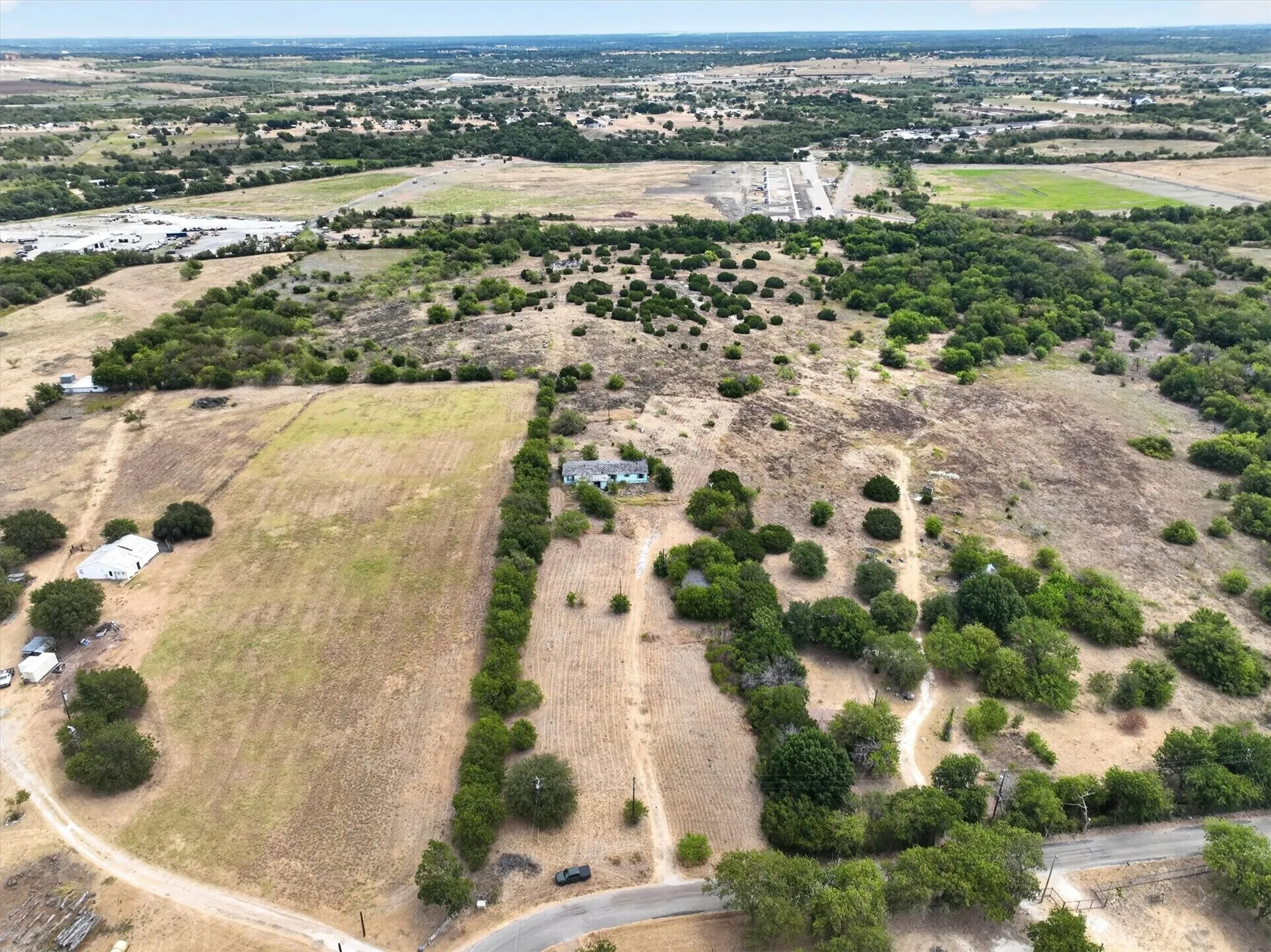 Expansive rural landscape featuring a single-story dwelling, varied terrain, scattered trees, and visible roadways