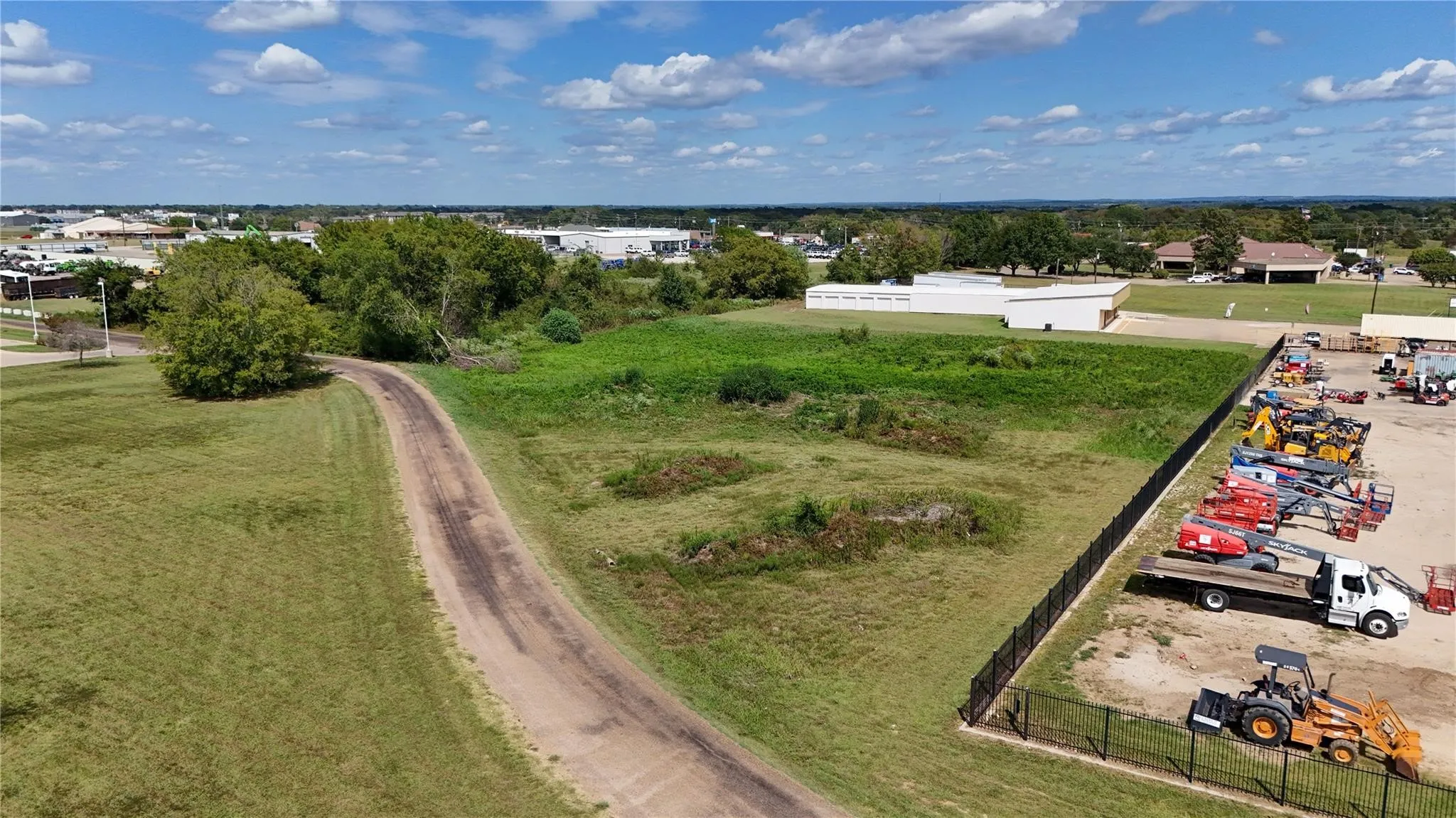 Expansive open land featuring a dirt access road, grassy areas, and mature trees