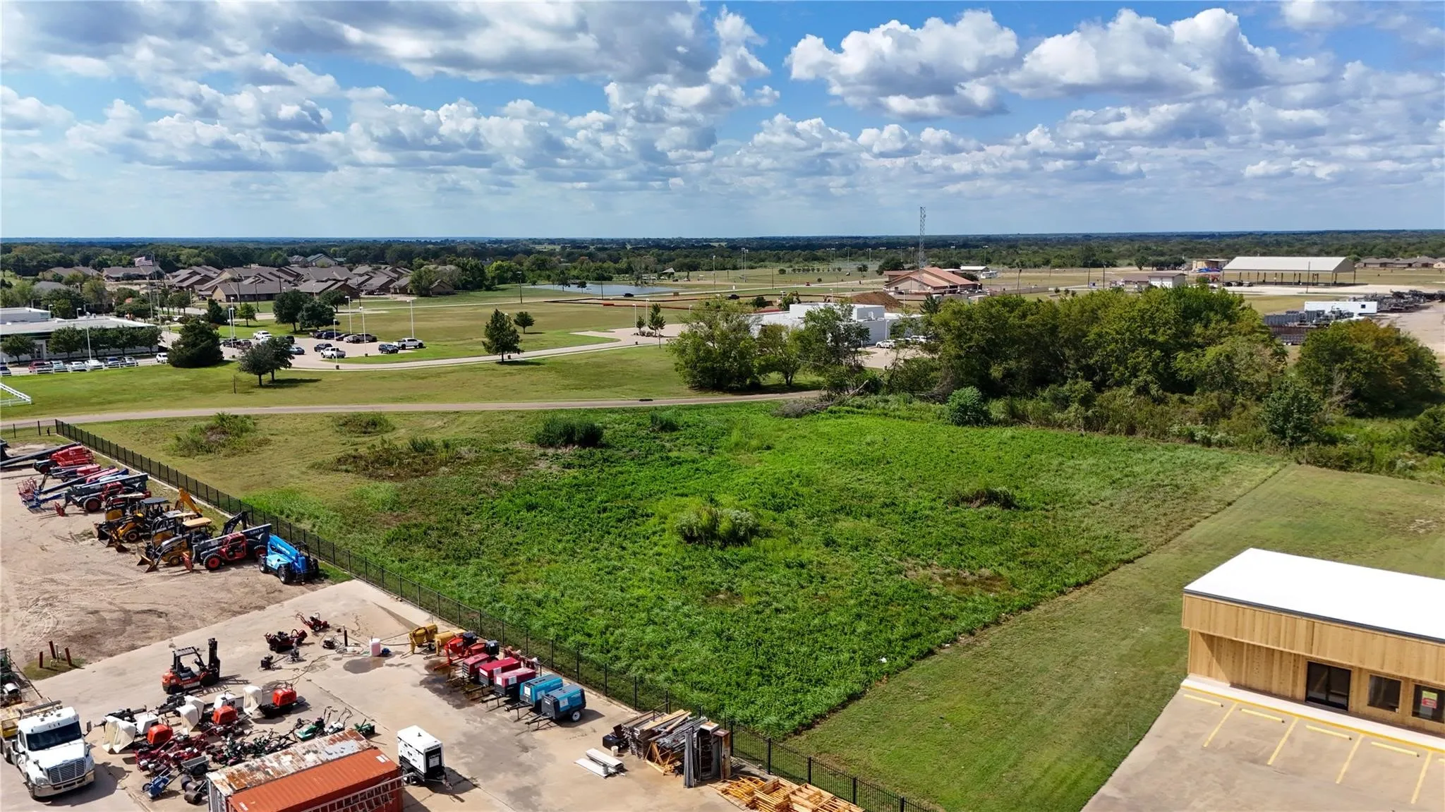 Expansive undeveloped parcel with established perimeter fencing, substantial green space, and surrounding commercial and residential areas