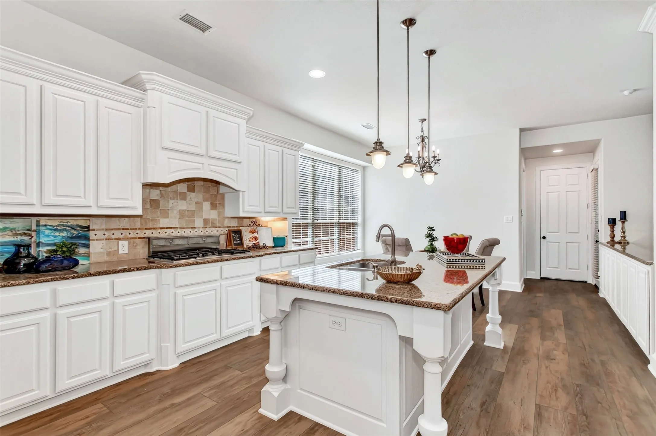 White cabinetry, wood-finish flooring, and a kitchen island with a built-in sink