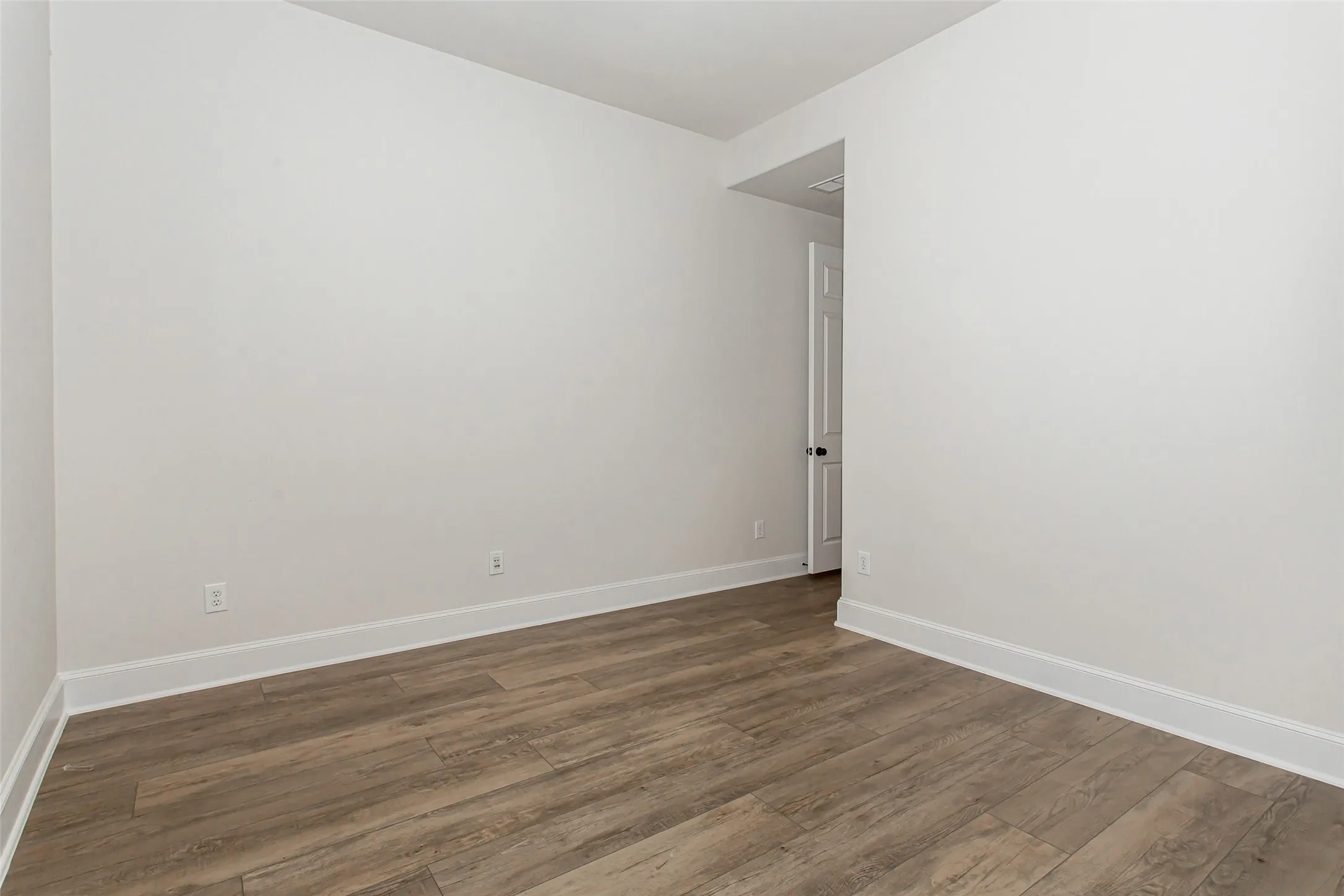 Room with wood-finish flooring, white walls, and a white door with a black knob