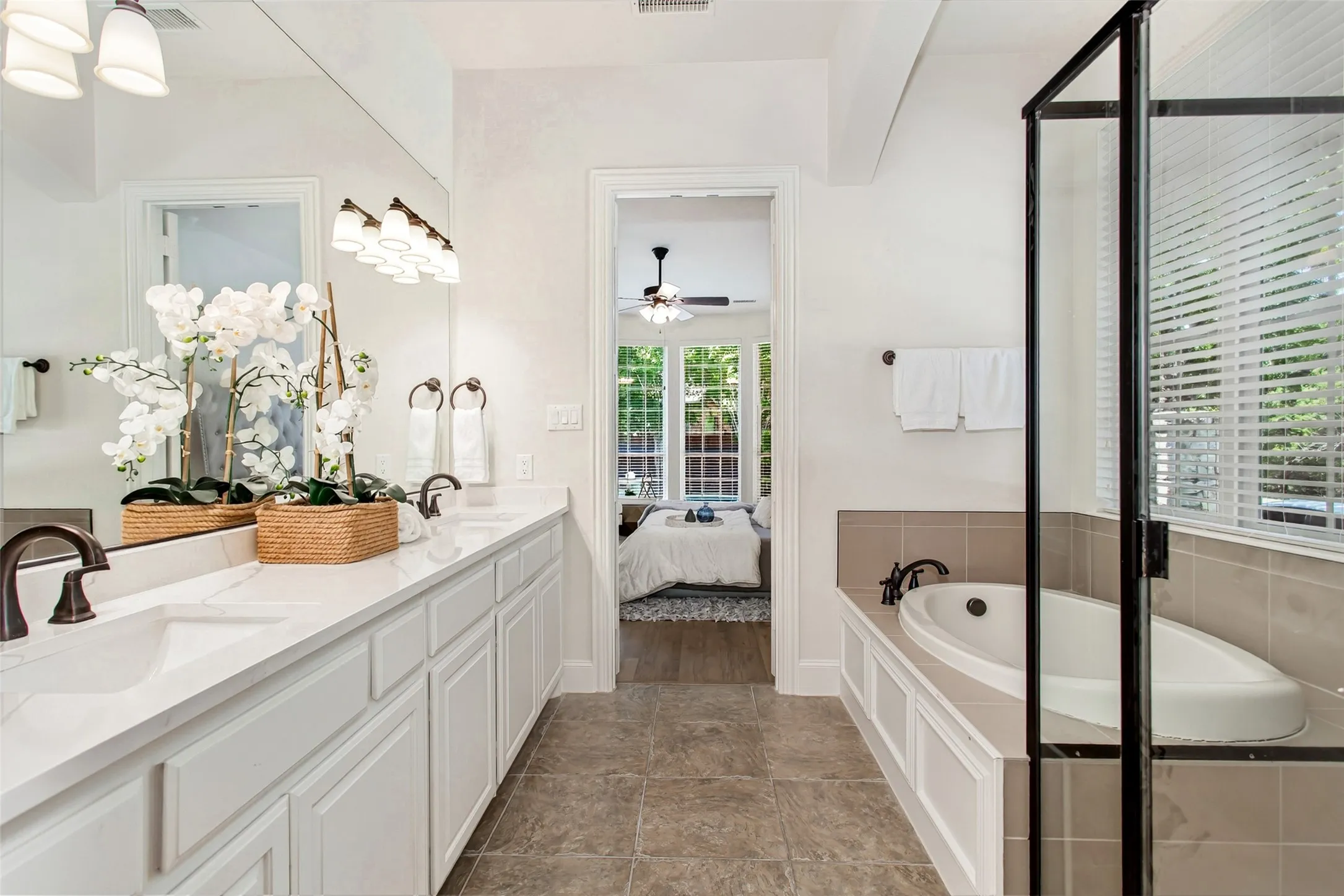 Dual vanity with white cabinetry and integrated sinks, a built-in soaking tub with tile surround, and a glass-enclosed shower