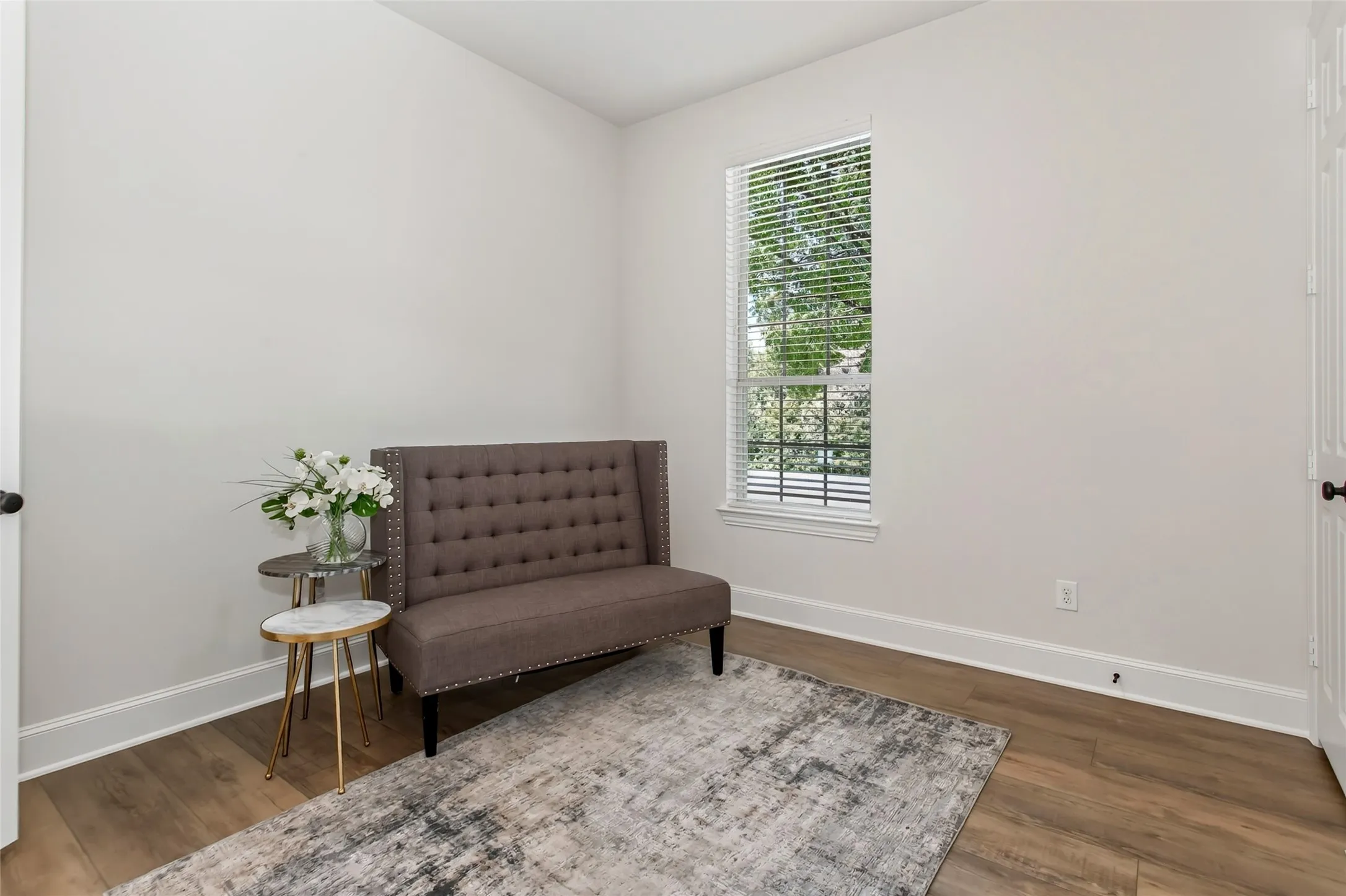 Wood-finish flooring throughout, bright window with blinds, white trim, and light wall color