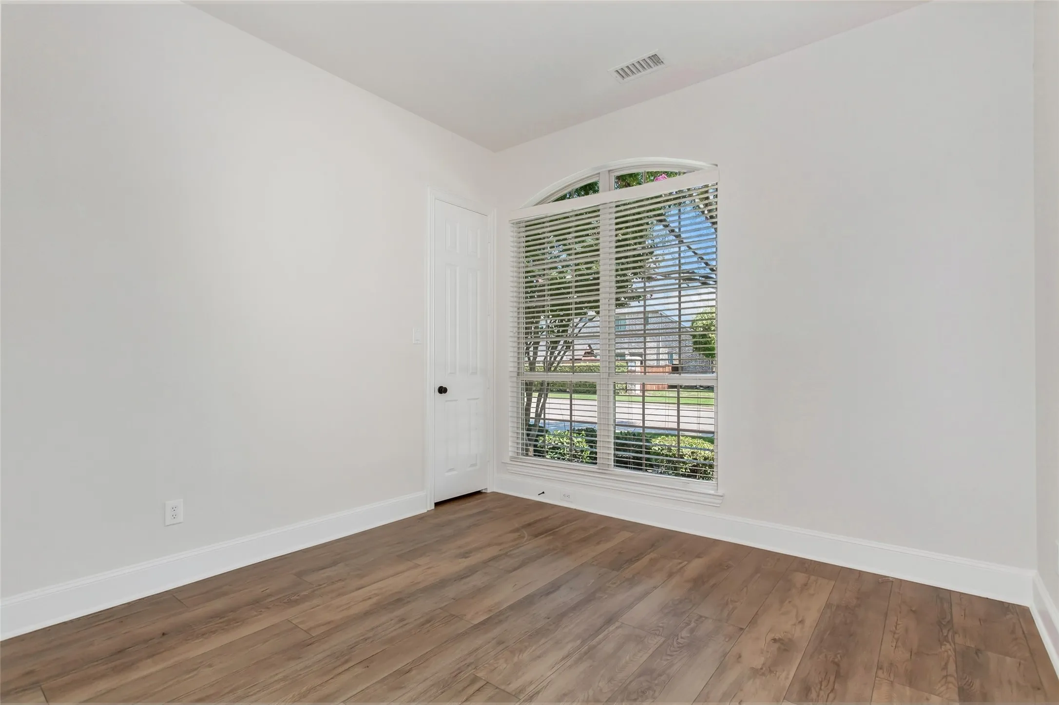 Arched window with blinds, wood-finish flooring, white walls, white trim, and a paneled door