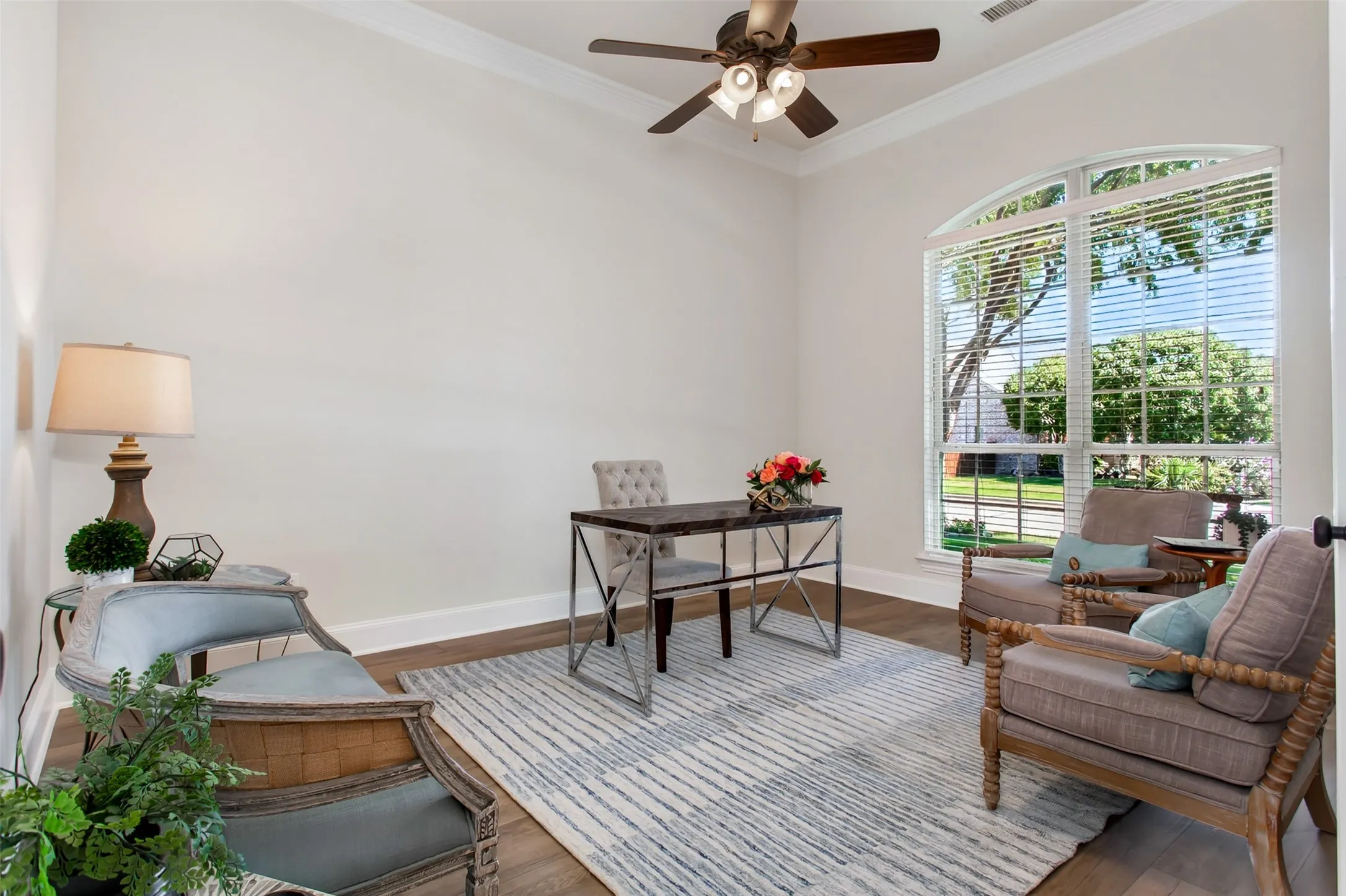 Arched window with blinds, wood-finish flooring, ceiling fan, crown molding, and neutral wall paint
