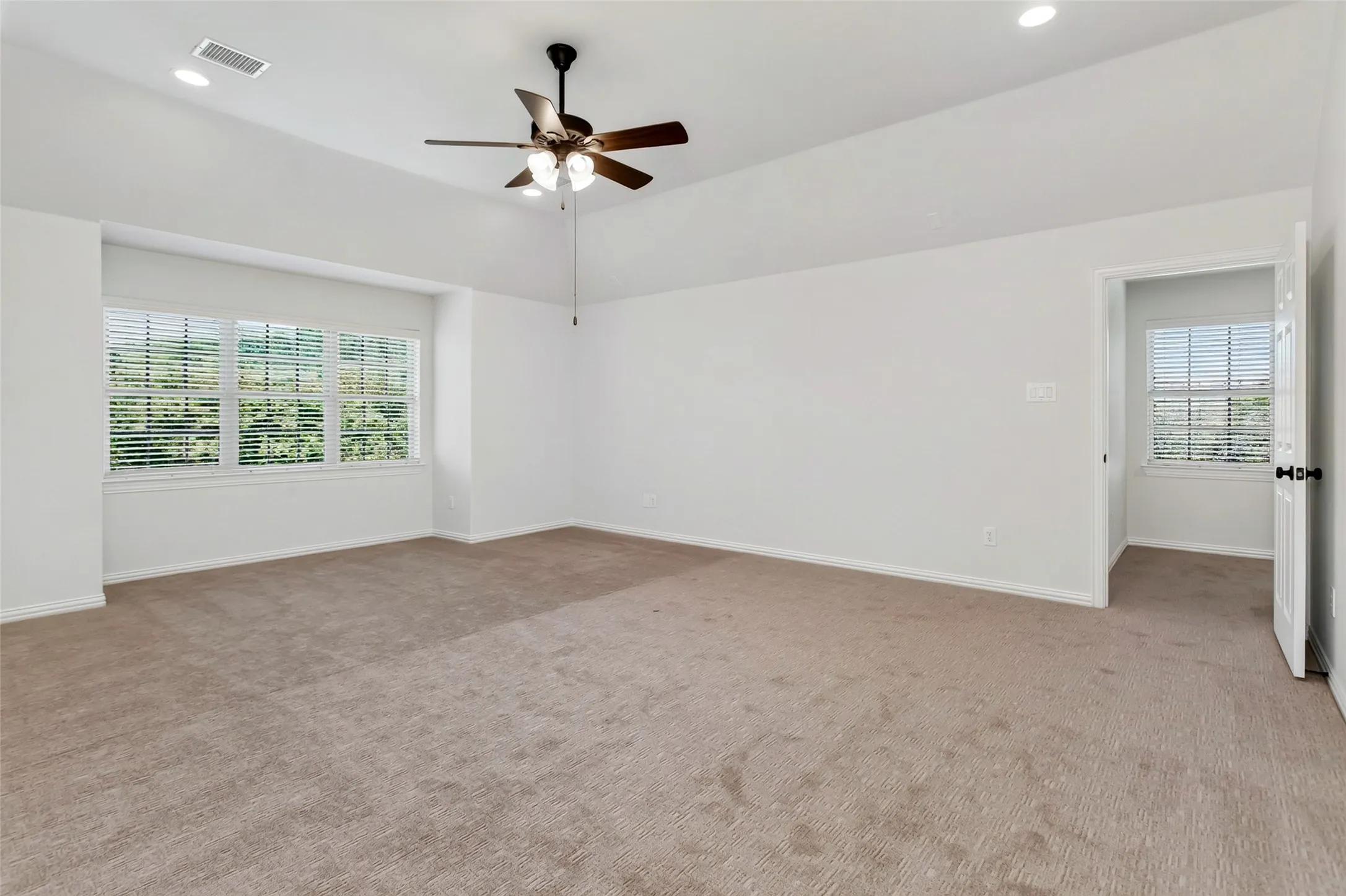 Spacious room featuring vaulted ceilings, recessed lighting, a ceiling fan, and multiple windows with blinds
