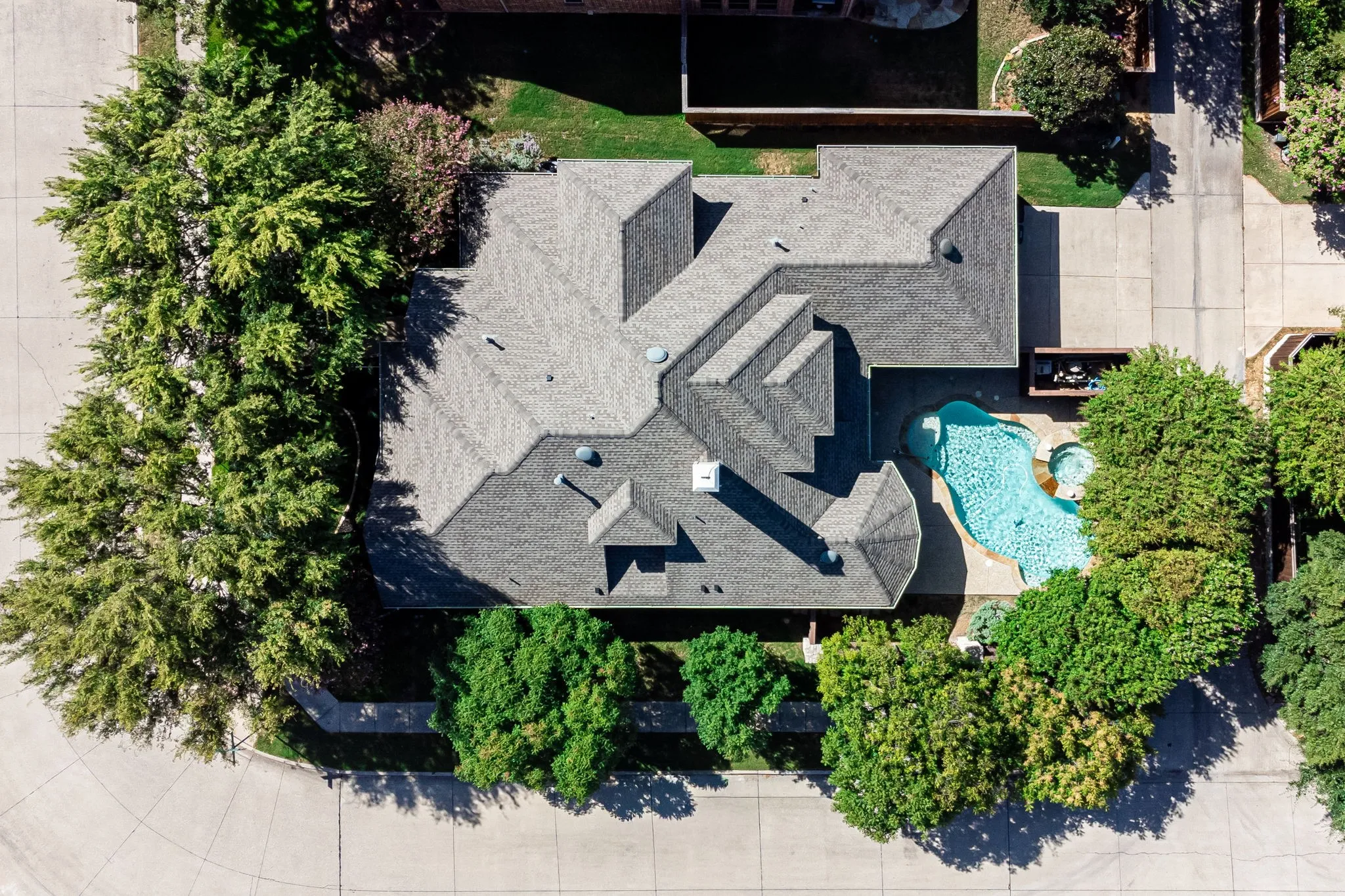 Pitched shingle roof, expansive pool, integrated spa, mature trees, and concrete driveway