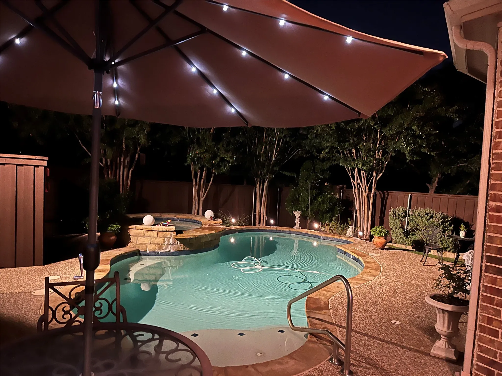 Custom-shaped swimming pool with an integrated spa, surrounded by stone coping and aggregate decking