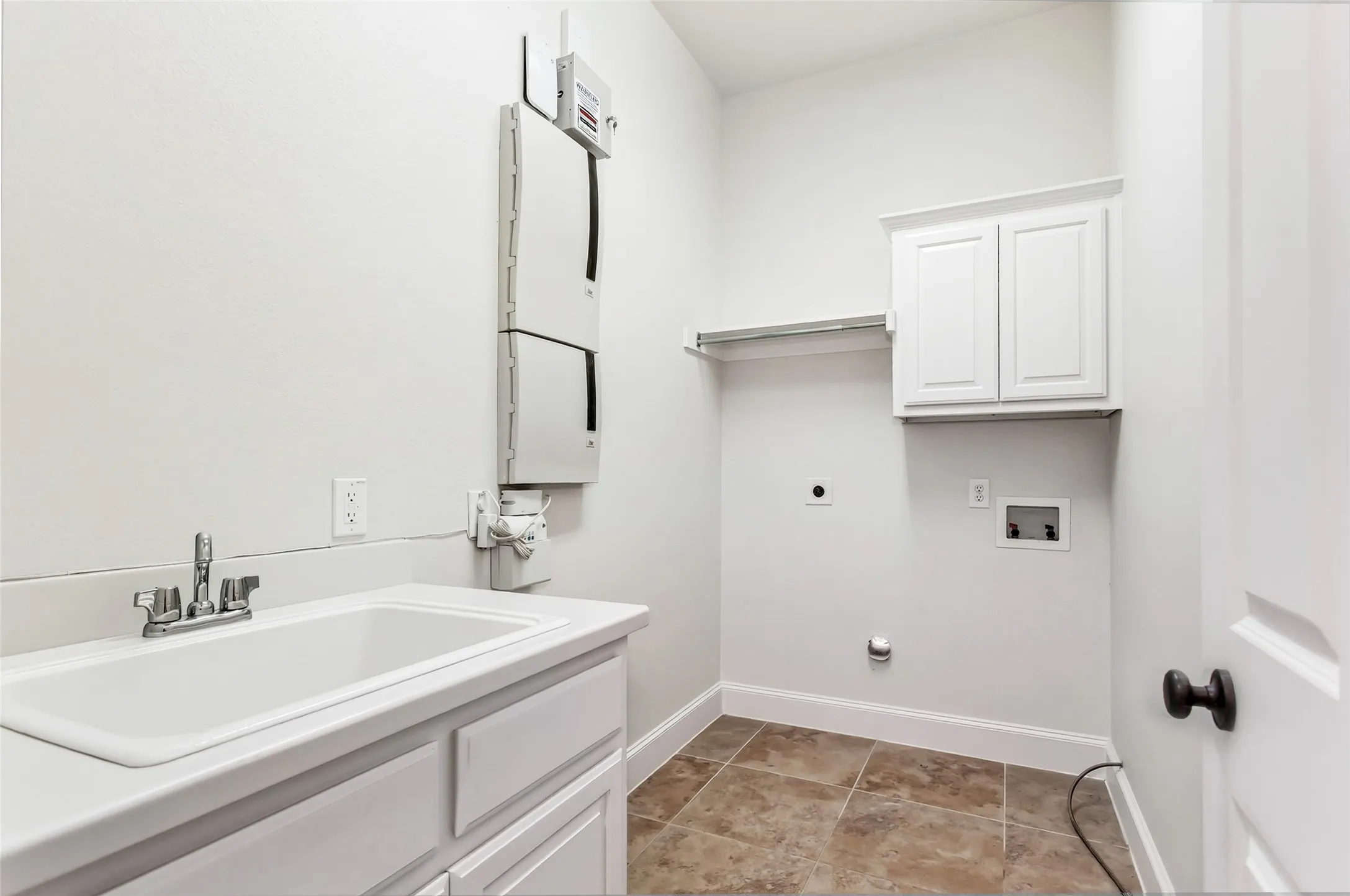 Utility sink with chrome faucet, built-in white cabinetry, shelving, and tile flooring