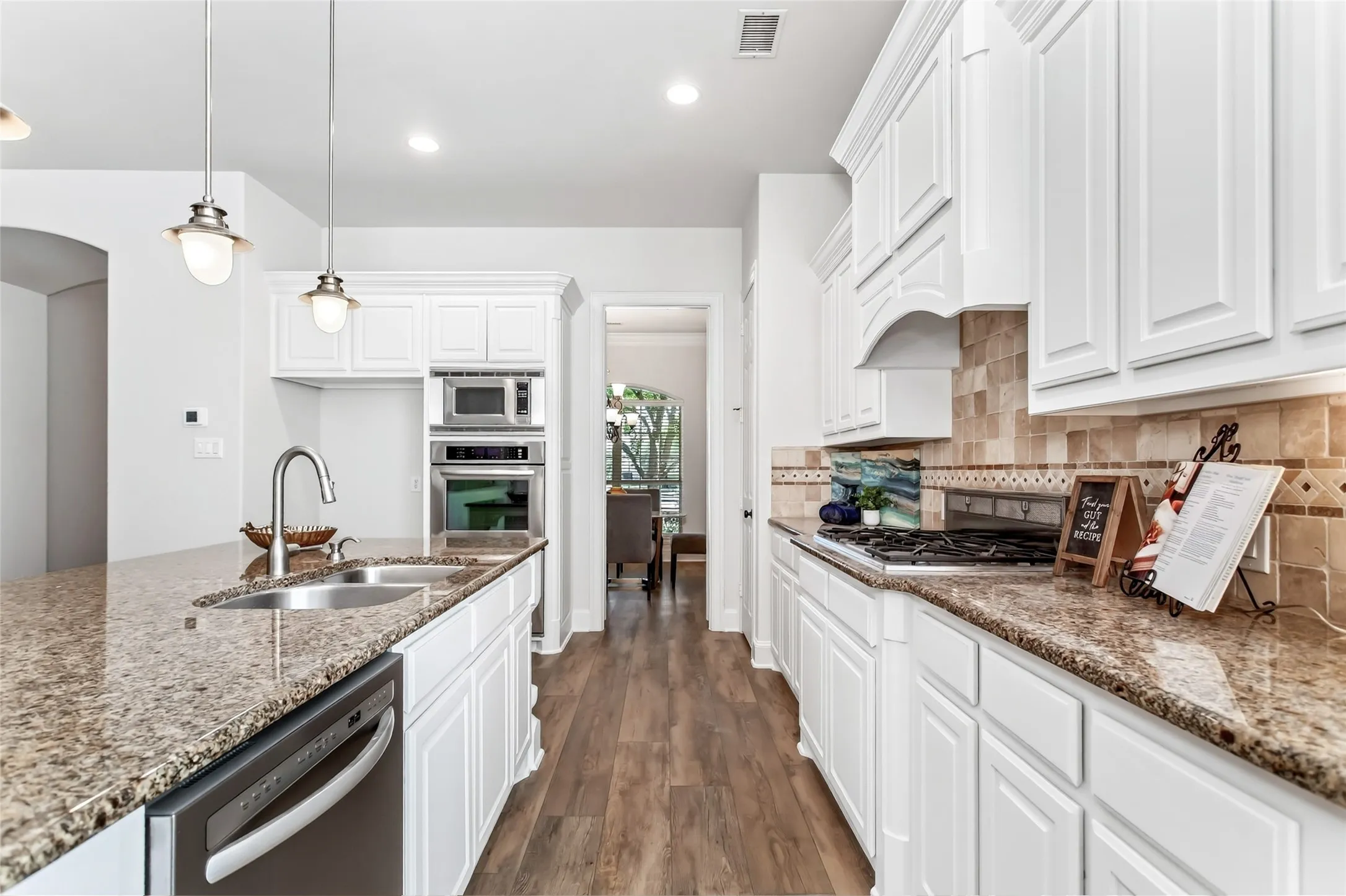 Kitchen featuring white cabinetry, wood-finish flooring, granite countertops, tile backsplash, and stainless steel appliances