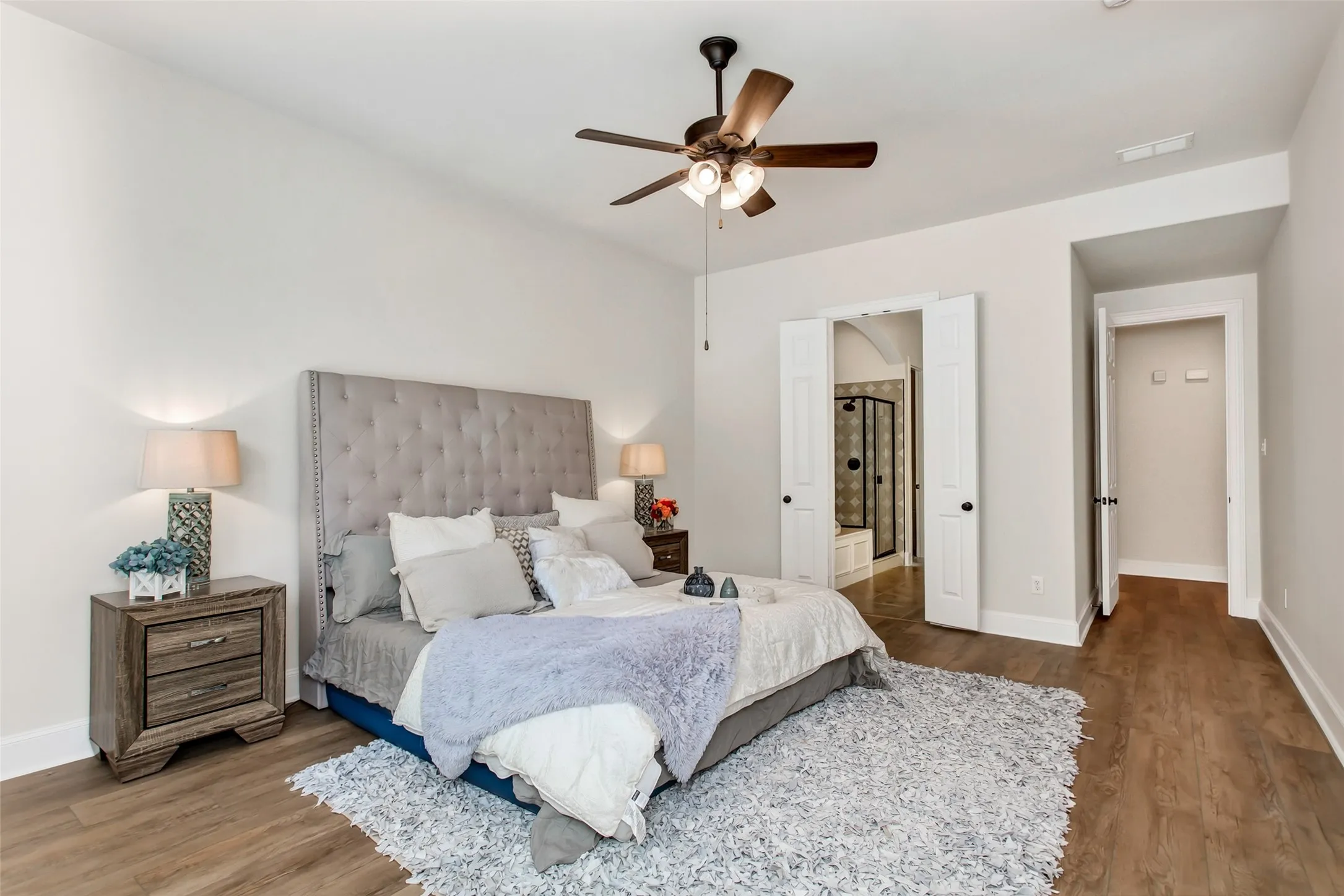 Wood-finish flooring, ceiling fan with integrated lighting, and an arched doorway leading to a tiled shower