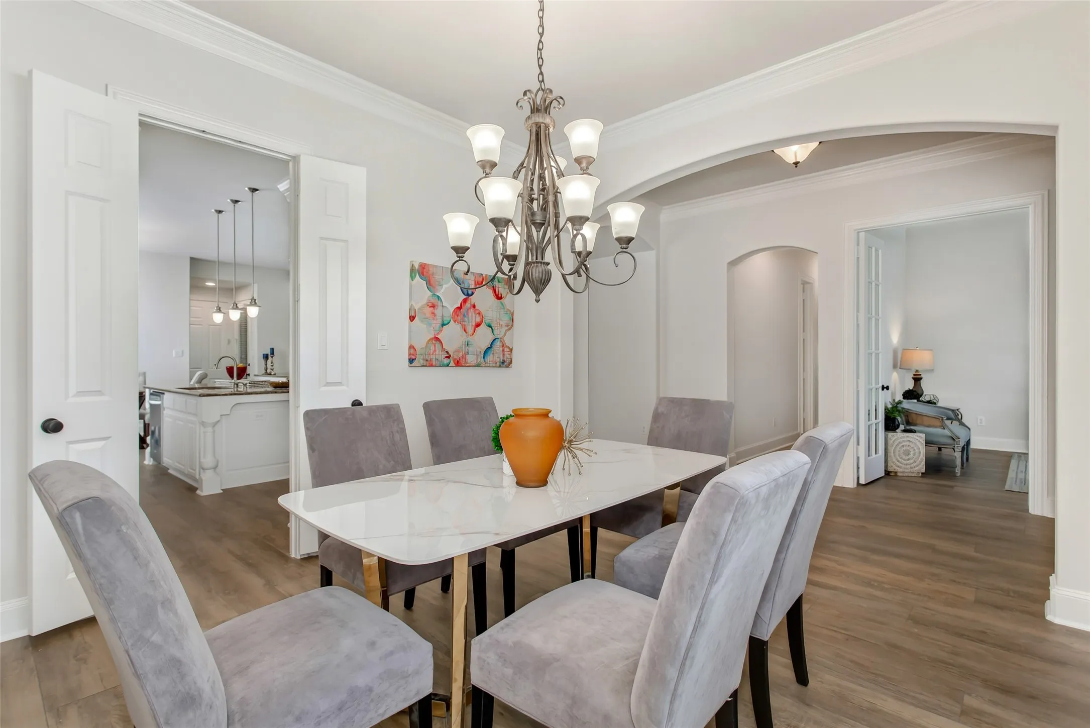 Dining area featuring wood-finish flooring, crown molding, a multi-light chandelier, and an arched doorway