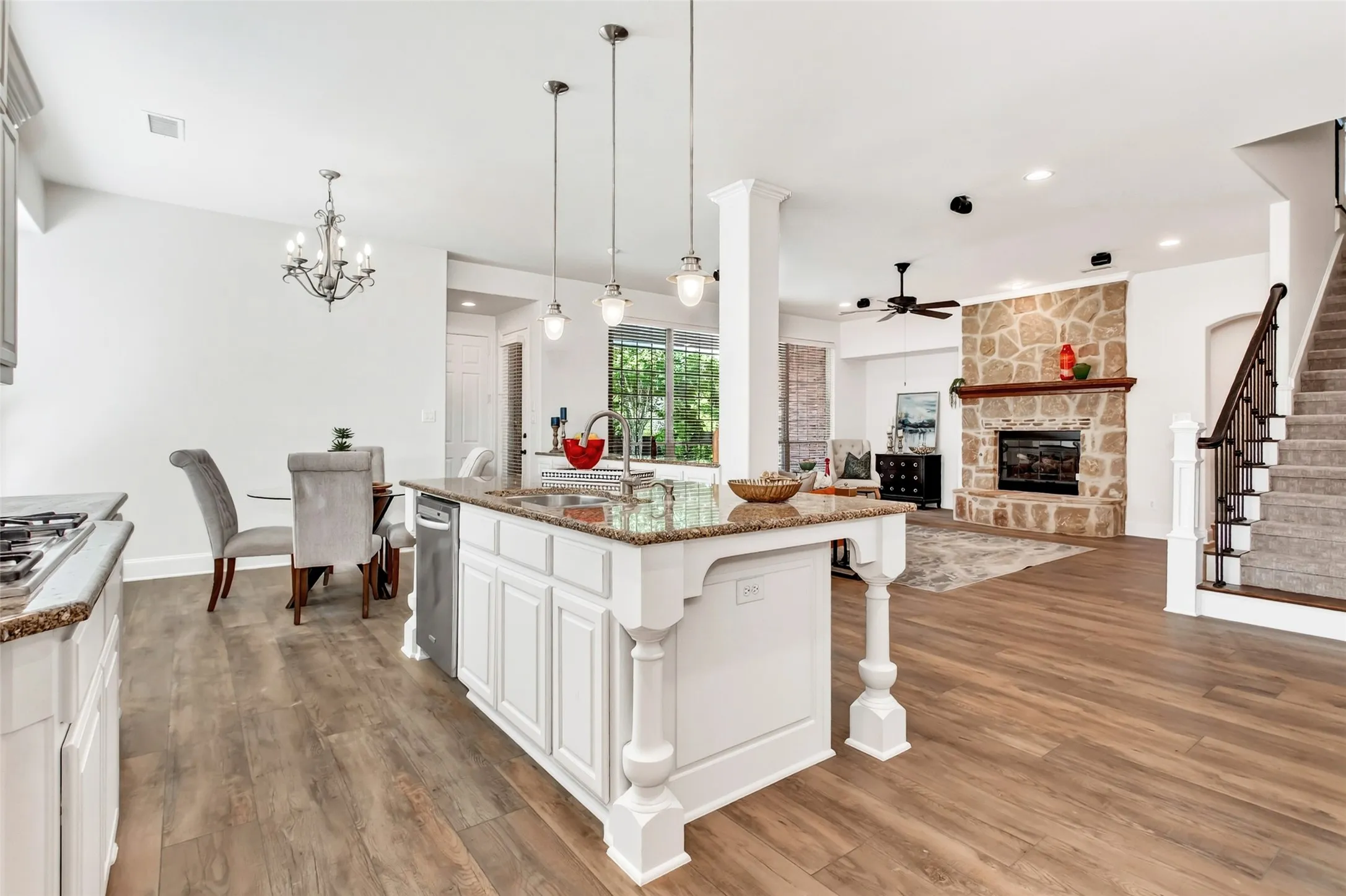 Kitchen island with granite countertop, wood-finish flooring, stone fireplace, and staircase with carpeted treads
