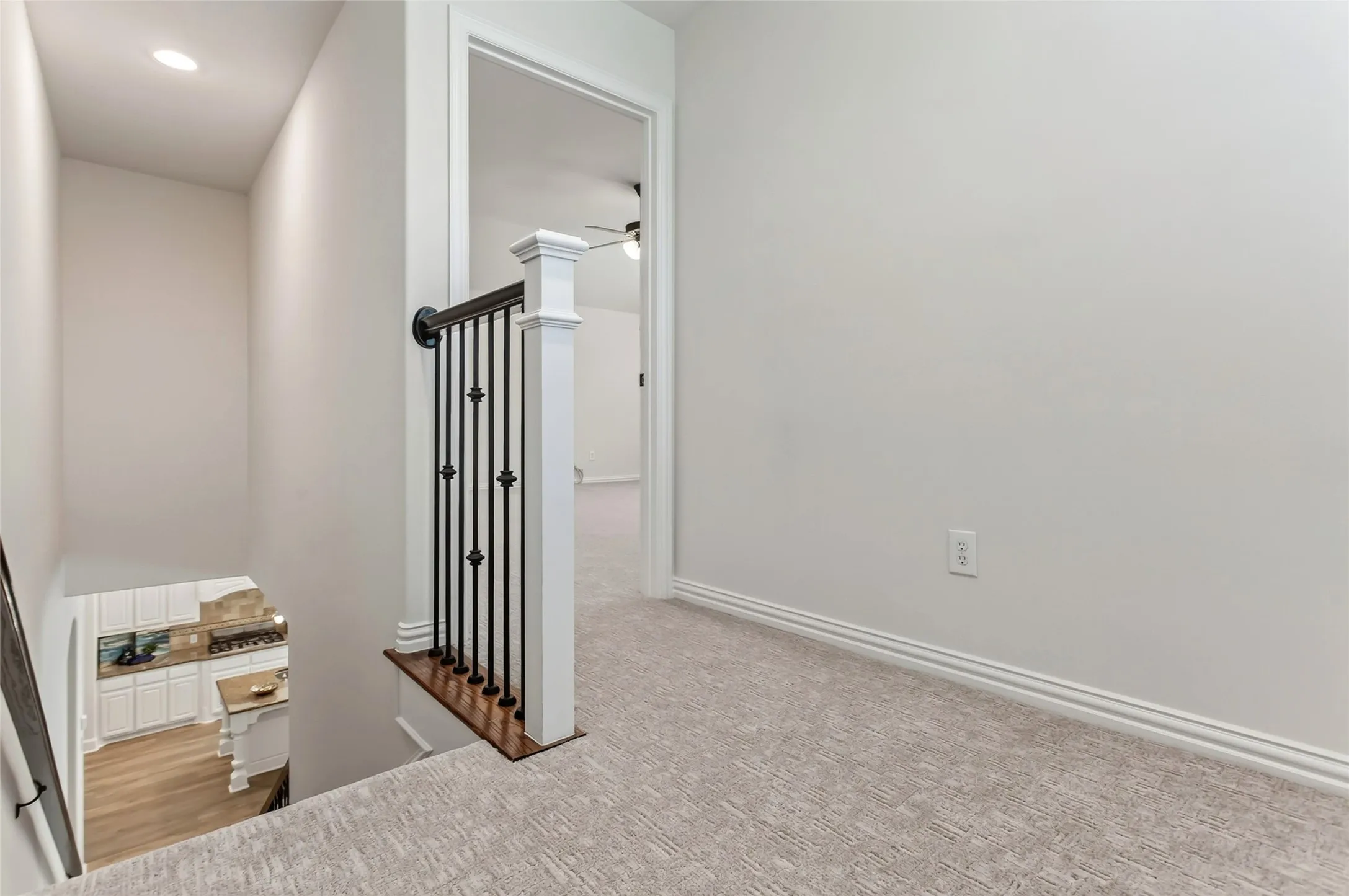Staircase featuring wrought iron balusters, wood-finish handrail, and carpeted landing