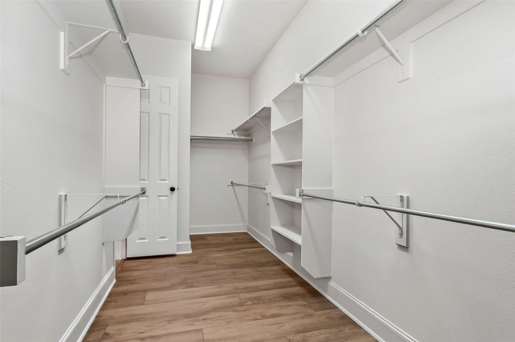 Walk-in closet featuring wood-finish flooring, white walls, built-in shelving, and multiple clothing rods