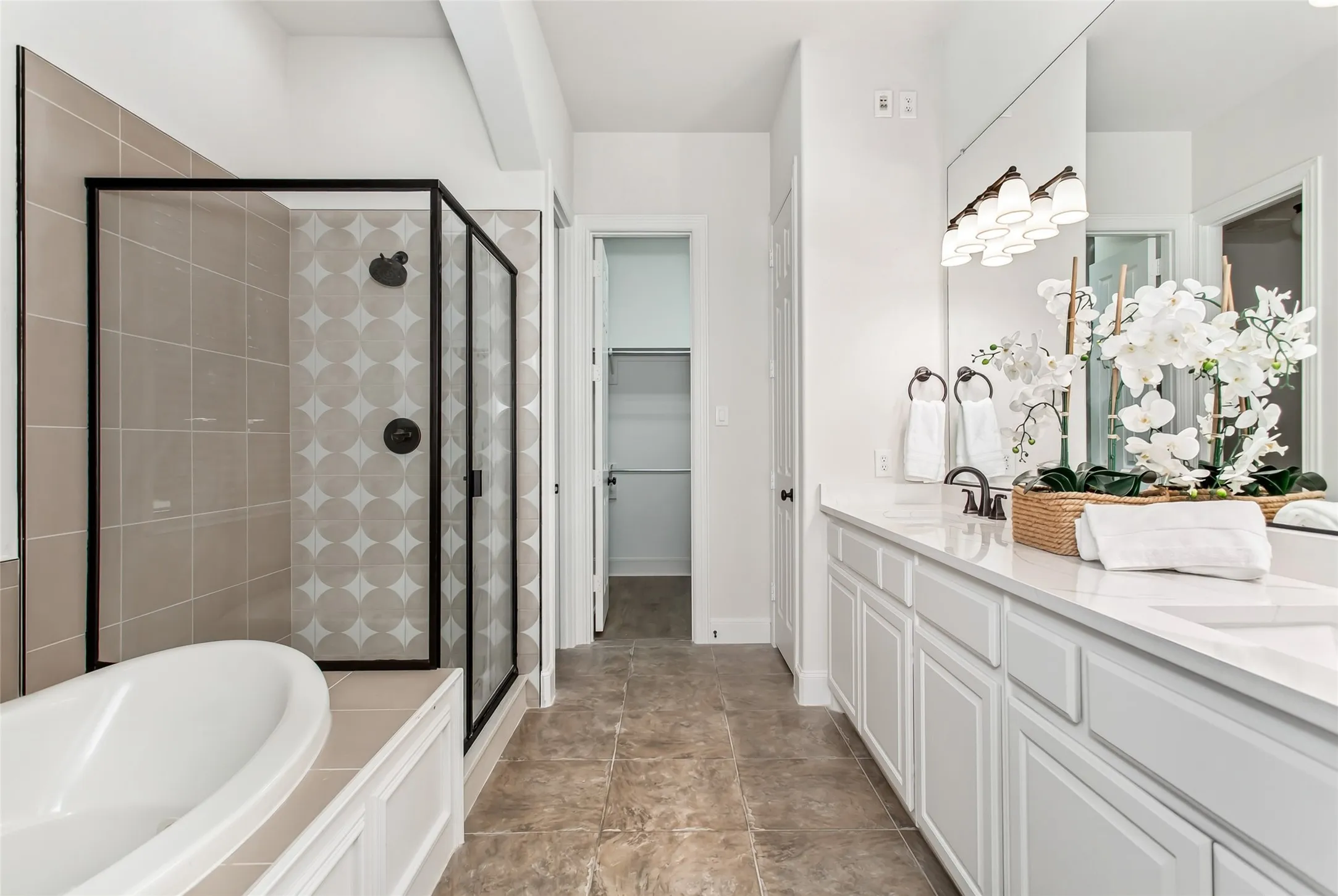 Bathroom featuring dual white vanities with integrated sinks, a black-framed glass shower enclosure, a built-in soaking tub, and tile flooring
