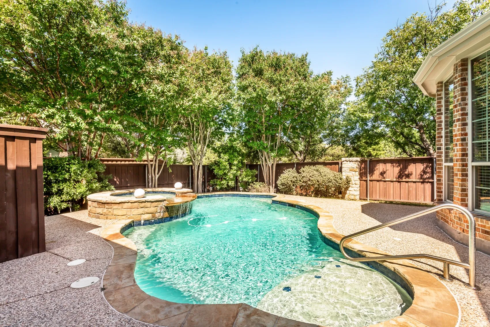 Curved swimming pool with an integrated spa, stone coping, and an aggregate deck