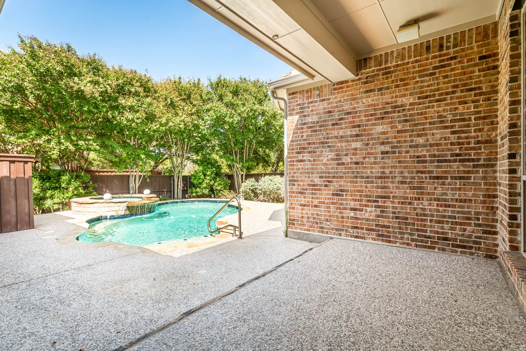 Private backyard oasis featuring a swimming pool, integrated spa with waterfall, and a spacious exposed aggregate patio