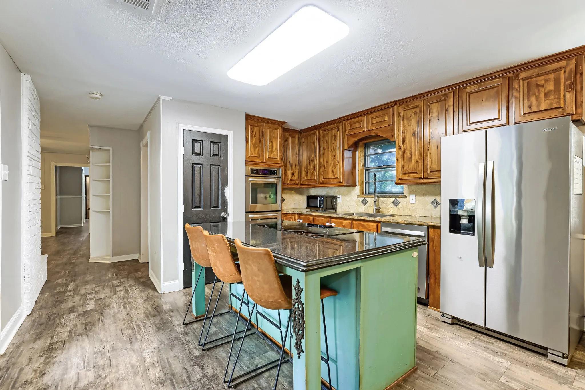 Kitchen featuring a central island with countertop seating, wood-finish flooring, built-in double ovens, and extensive wood cabinetry