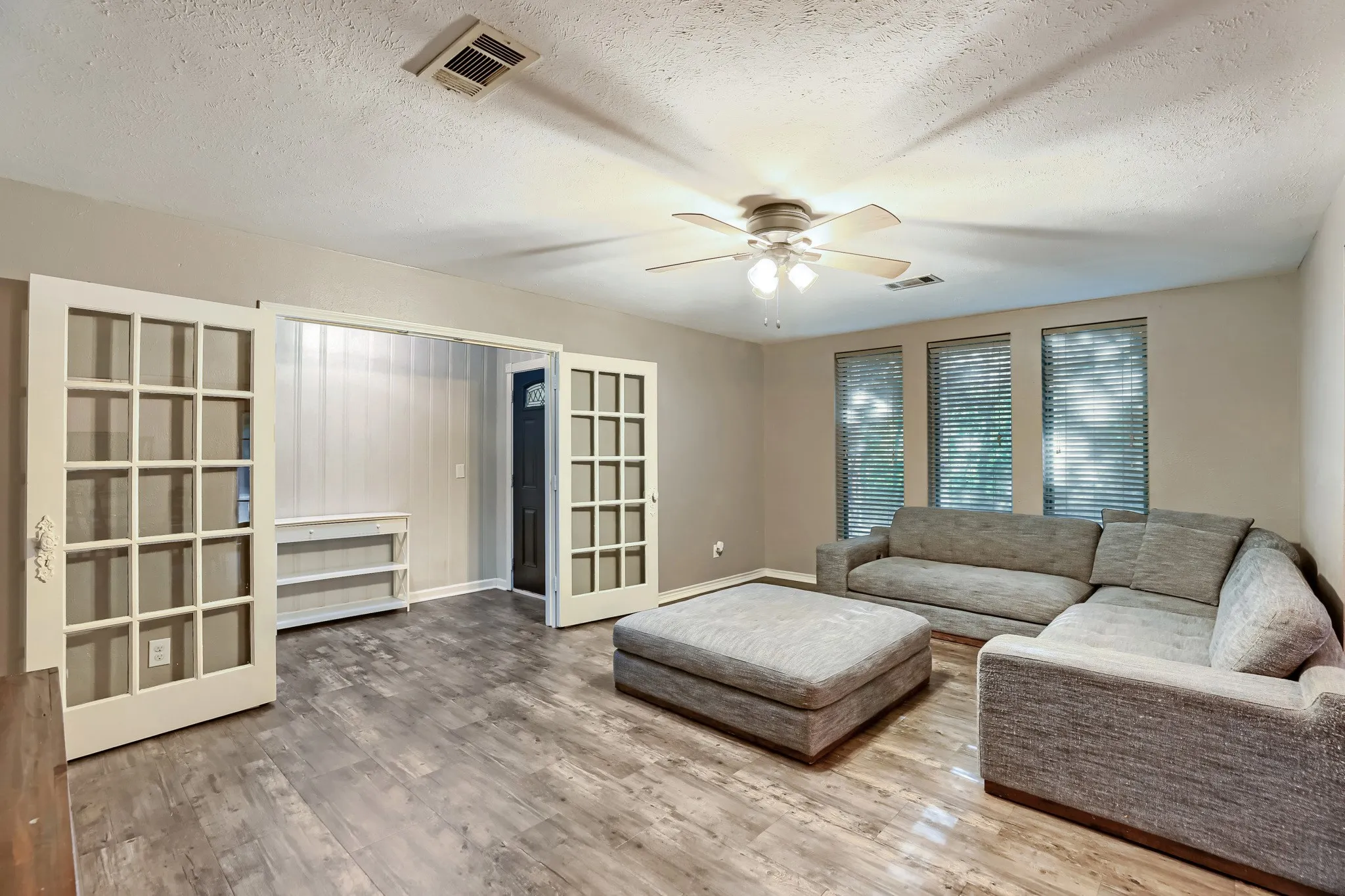 Wood-finish flooring, ceiling fan with integrated lighting, multiple windows with blinds, and paneled French doors