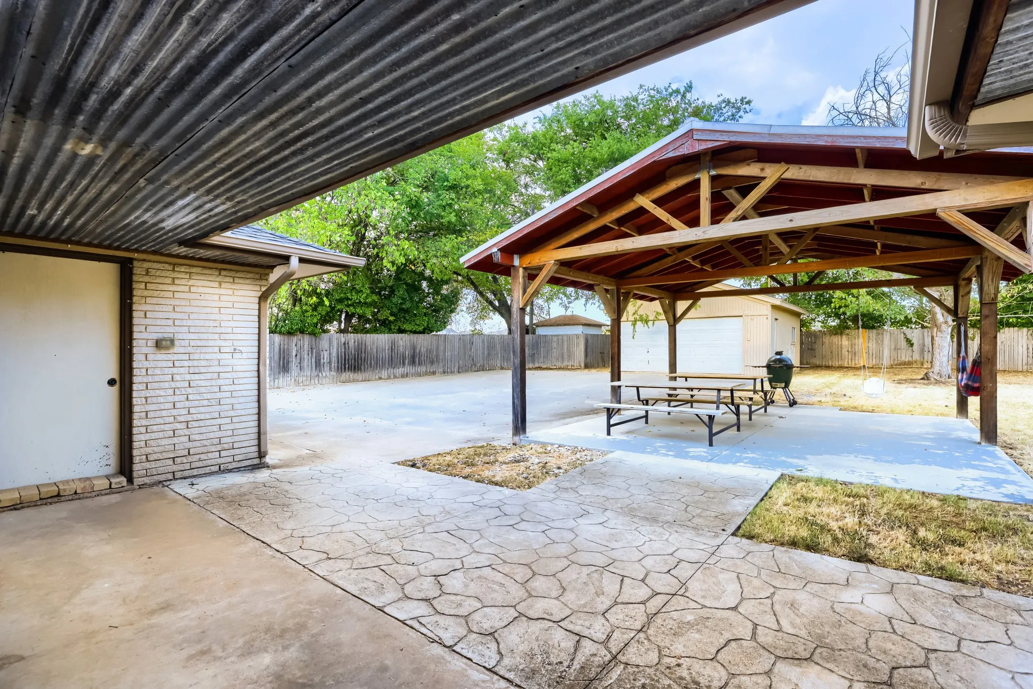 Covered patio with corrugated metal roofing, stamped concrete pathway, brick exterior, and a separate covered pavilion structure