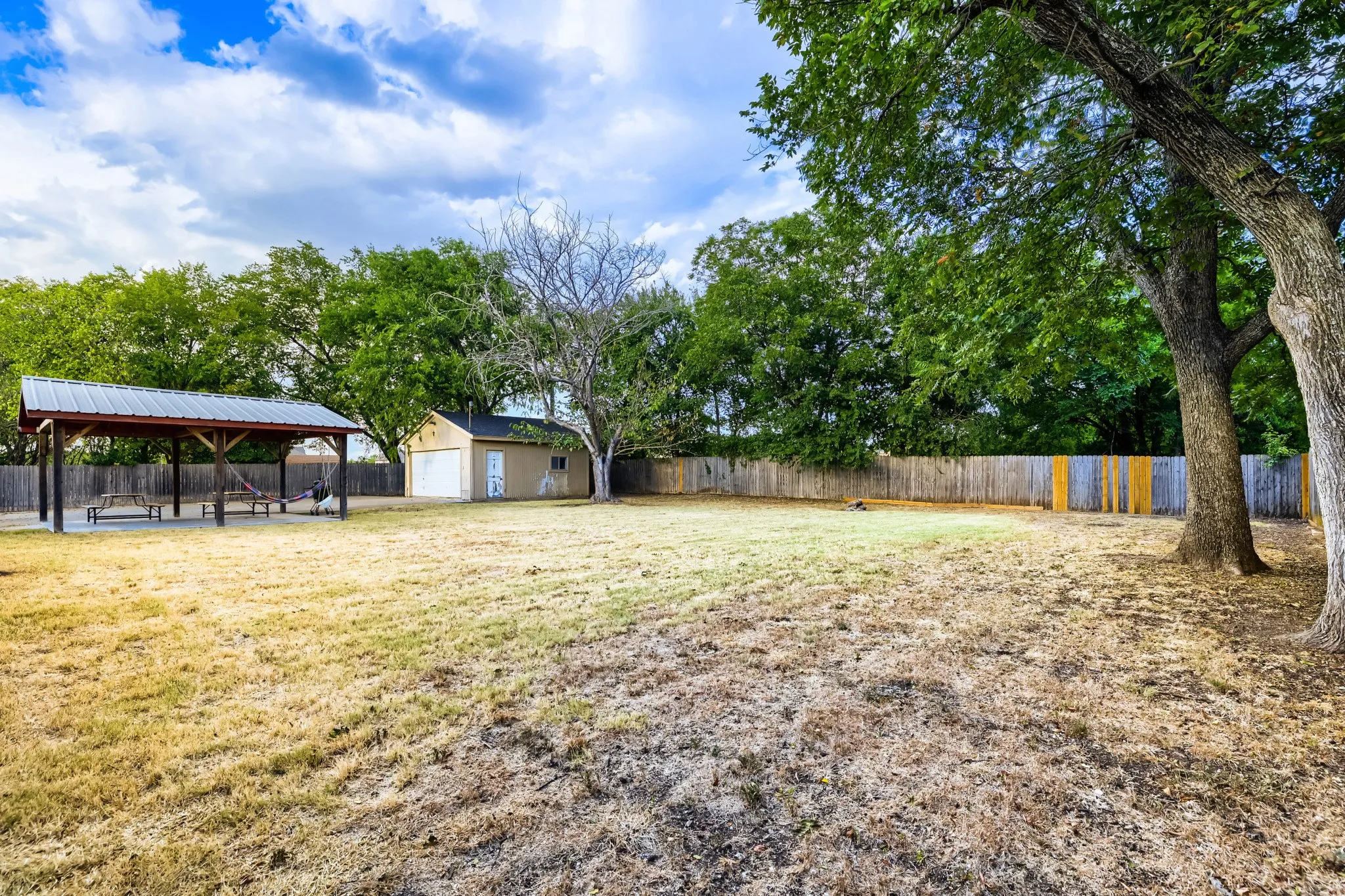 Expansive property featuring a detached shed, a covered outdoor structure with a metal roof, and a wood privacy fence