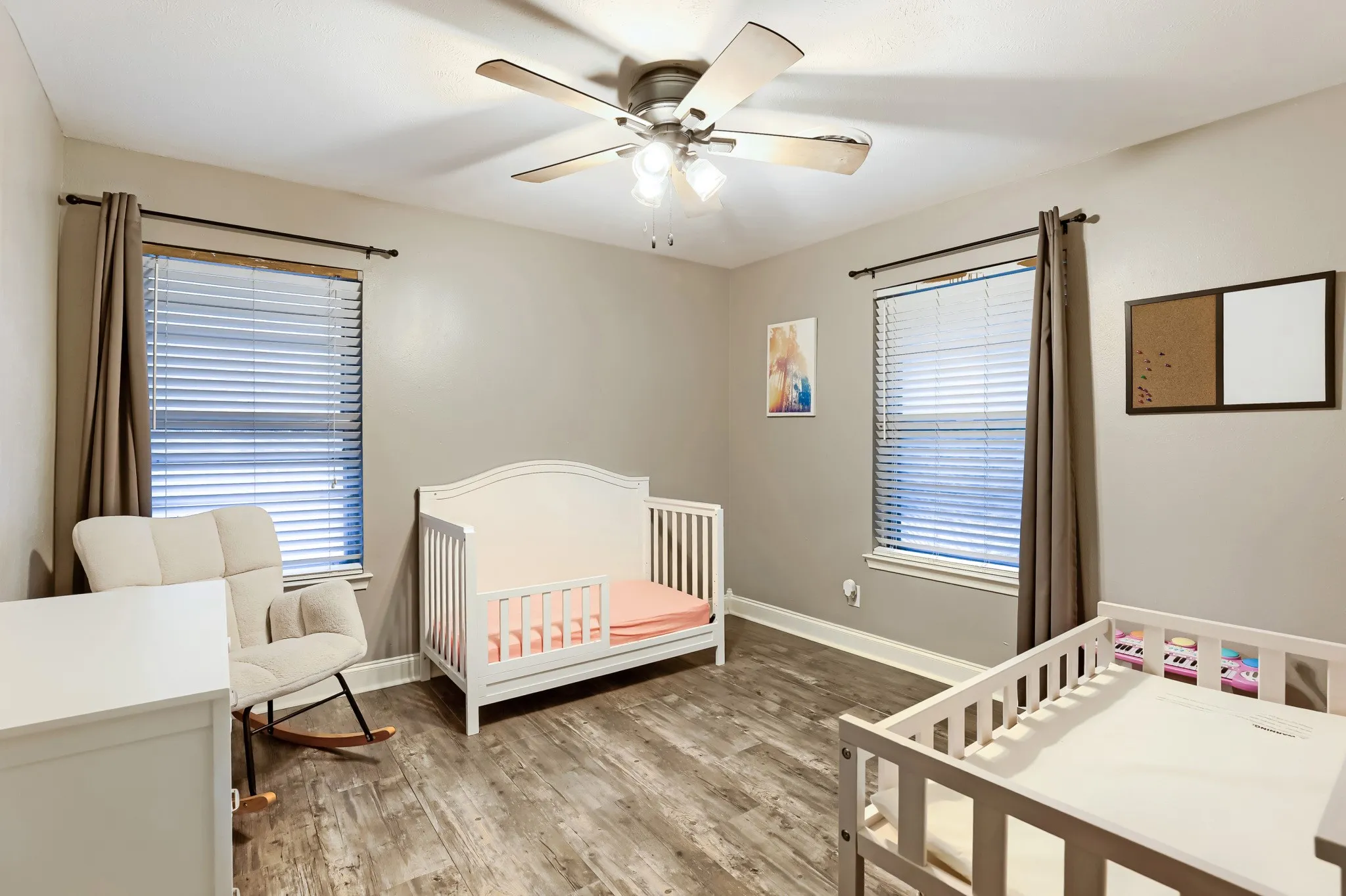 Wood-finish flooring, two windows with blinds, and an overhead ceiling fan with lighting