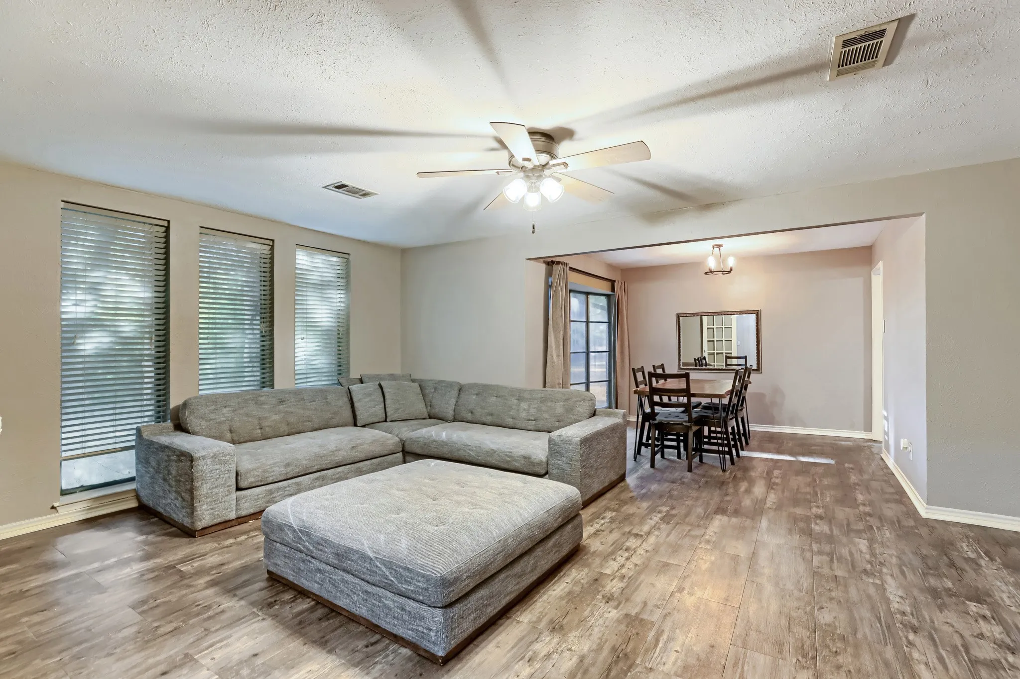 Wood-finish flooring, multiple windows with blinds, ceiling fan, and framed opening to an additional room