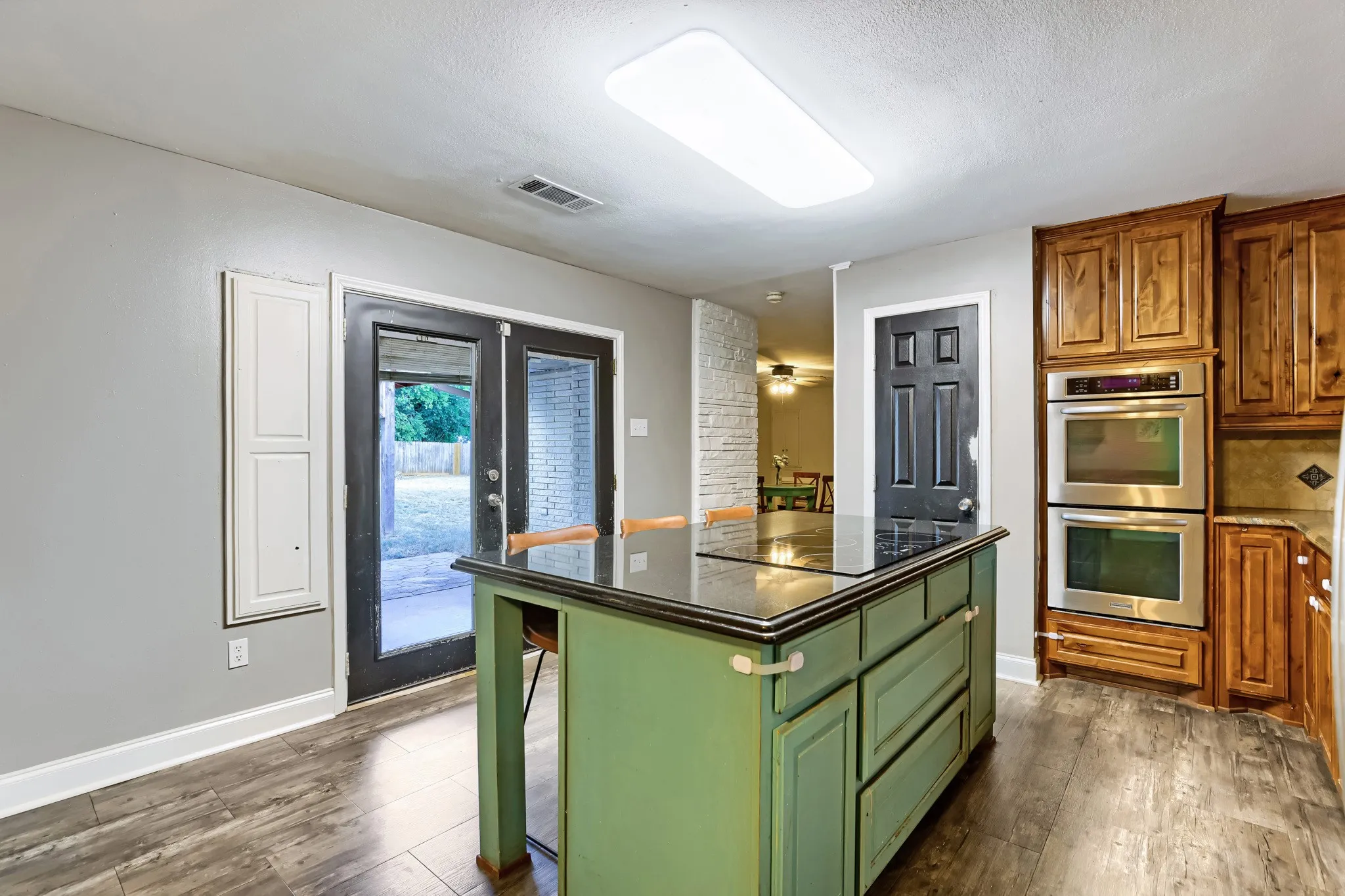 Kitchen featuring a center island with a dark countertop, wood-finish flooring, double wall ovens, and wood cabinetry