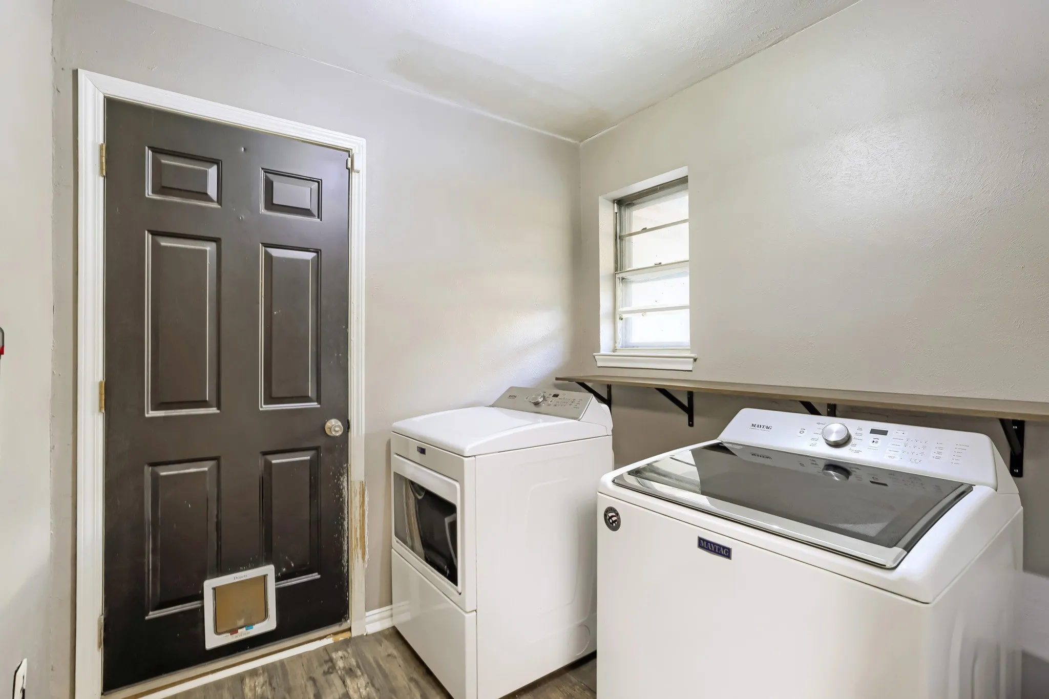 Utility area featuring wood-finish flooring, a functional window, and a built-in wood-finish shelf with black support brackets